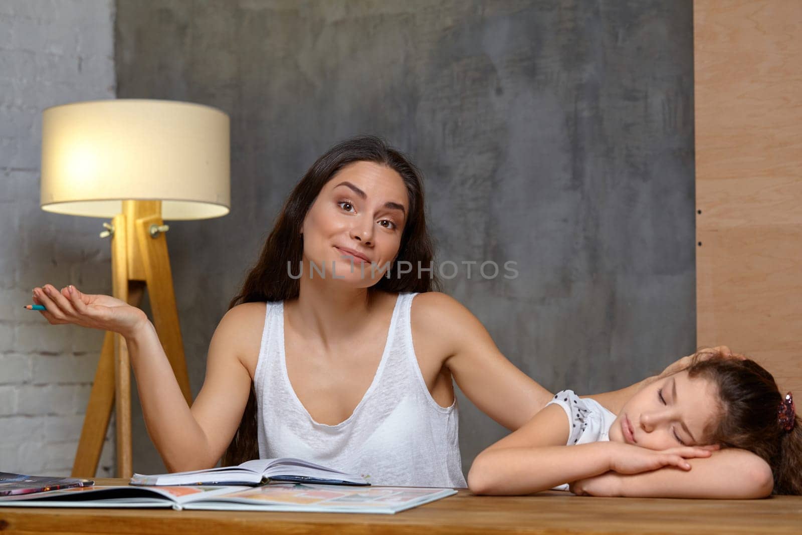 Portrait of a mother helping her small sweet and cute daughter to make her homework indoors. Mom is stroking her daughter and gesticulating, daughter is sleeping.