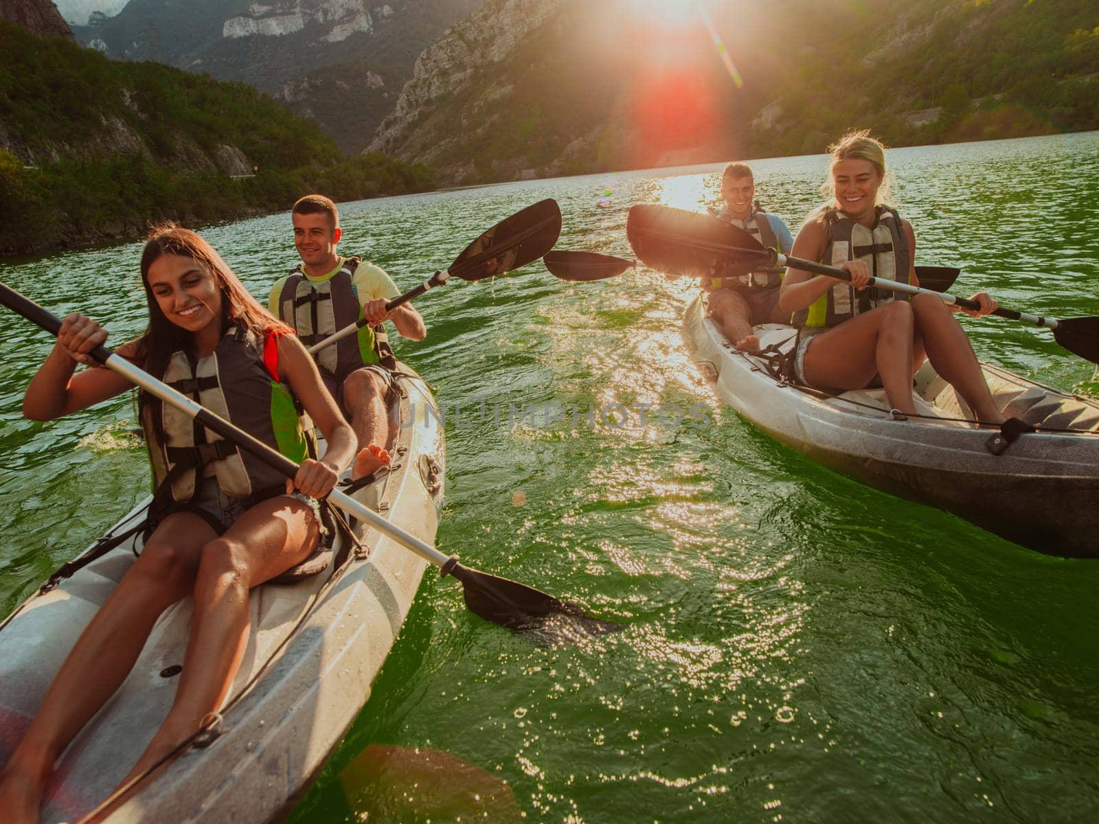 A group of friends enjoying fun and kayaking exploring the calm river, surrounding forest and large natural river canyons during an idyllic sunset. by dotshock