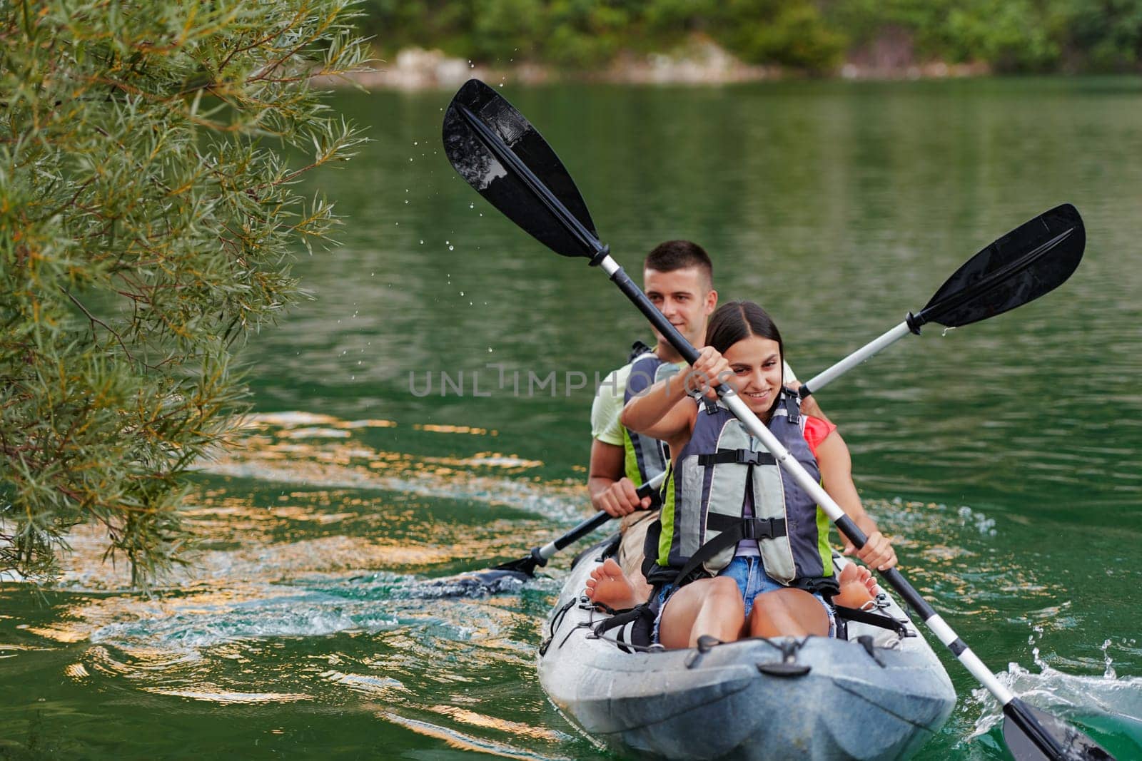 A young couple enjoying an idyllic kayak ride in the middle of a beautiful river surrounded by forest greenery.