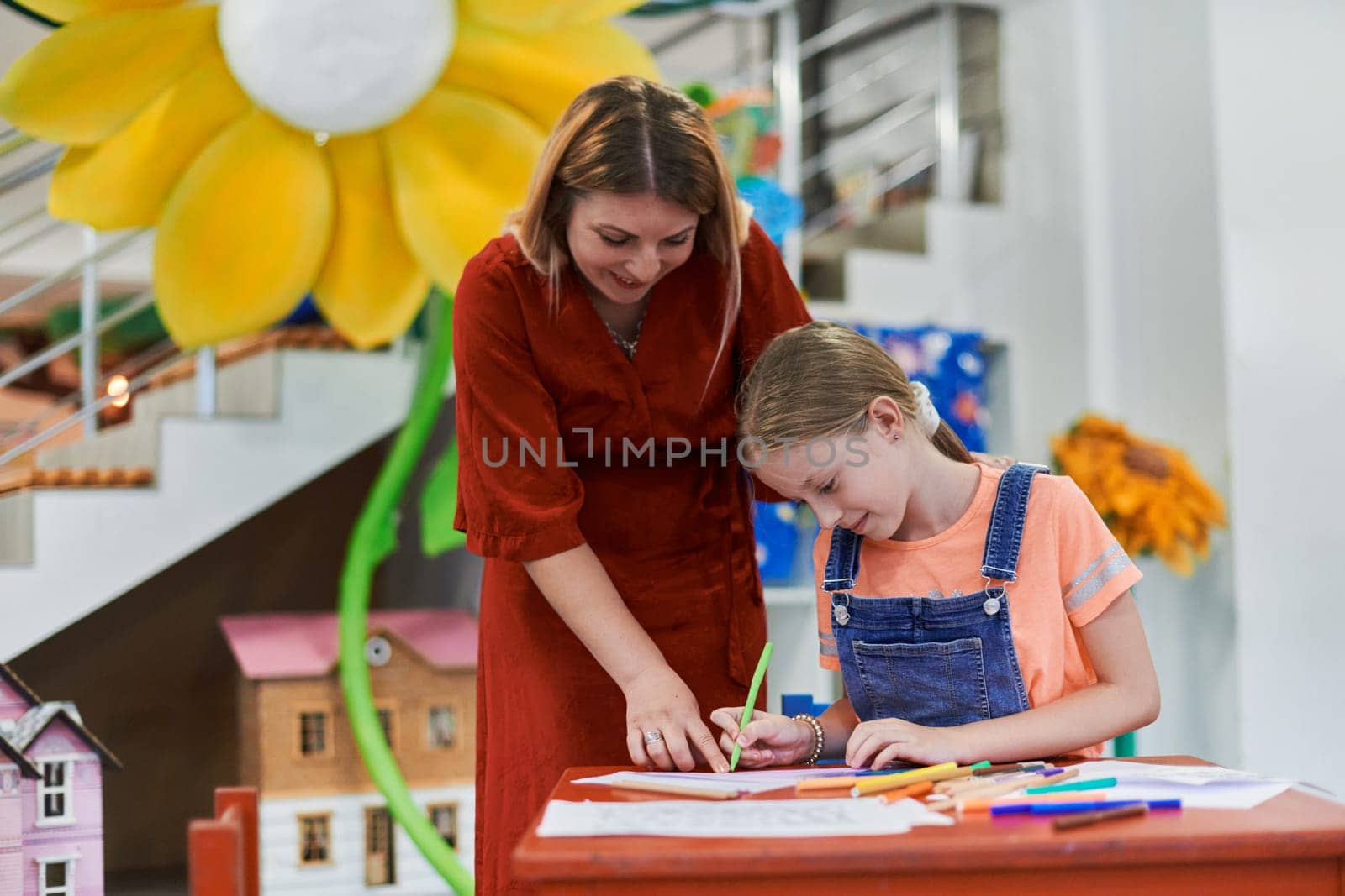 Creative kids during an art class in a daycare center or elementary school classroom drawing with female teacher. High quality photo