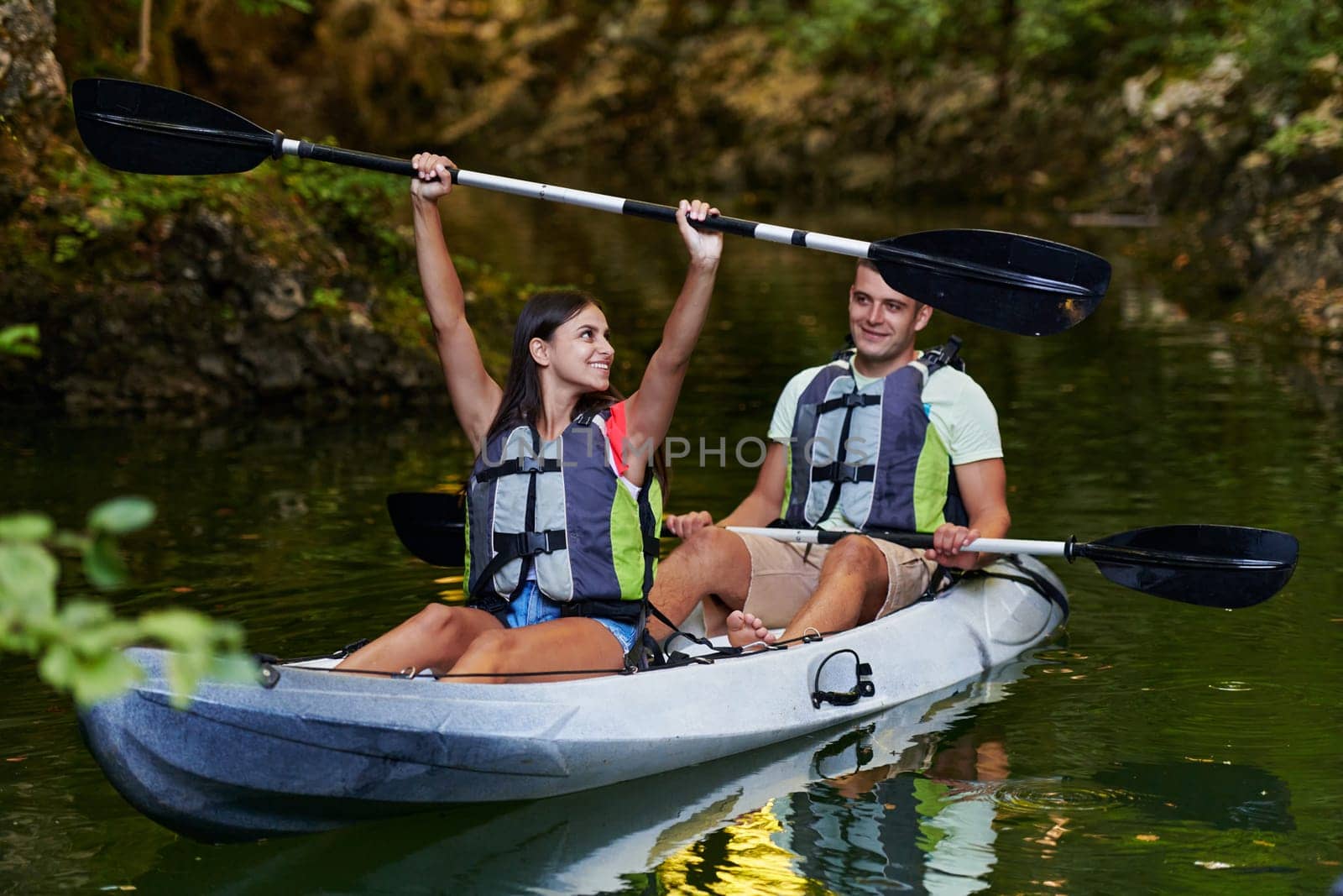 A young couple enjoying an idyllic kayak ride in the middle of a beautiful river surrounded by forest greenery by dotshock