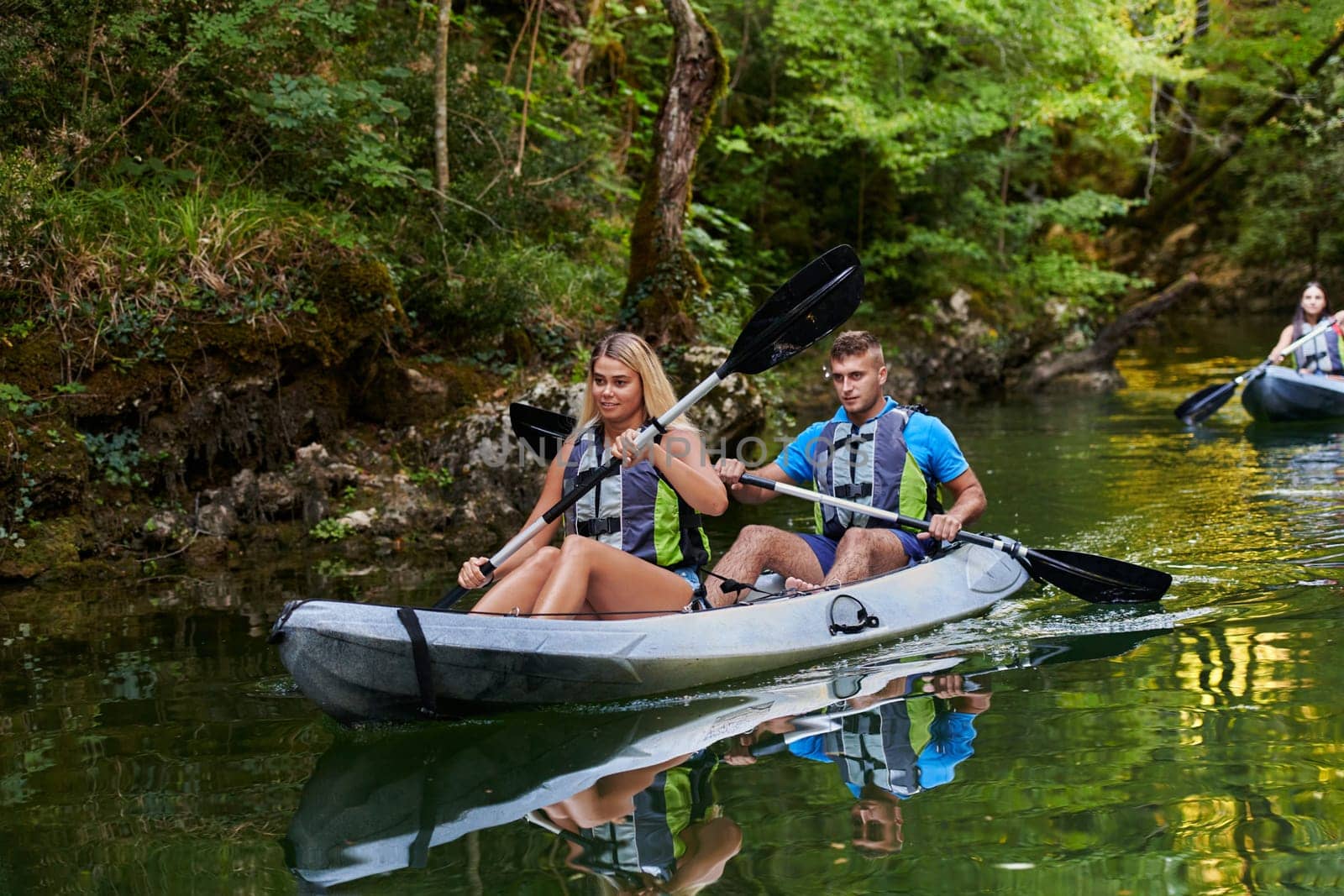 A group of friends enjoying having fun and kayaking while exploring the calm river, surrounding forest and large natural river canyons by dotshock