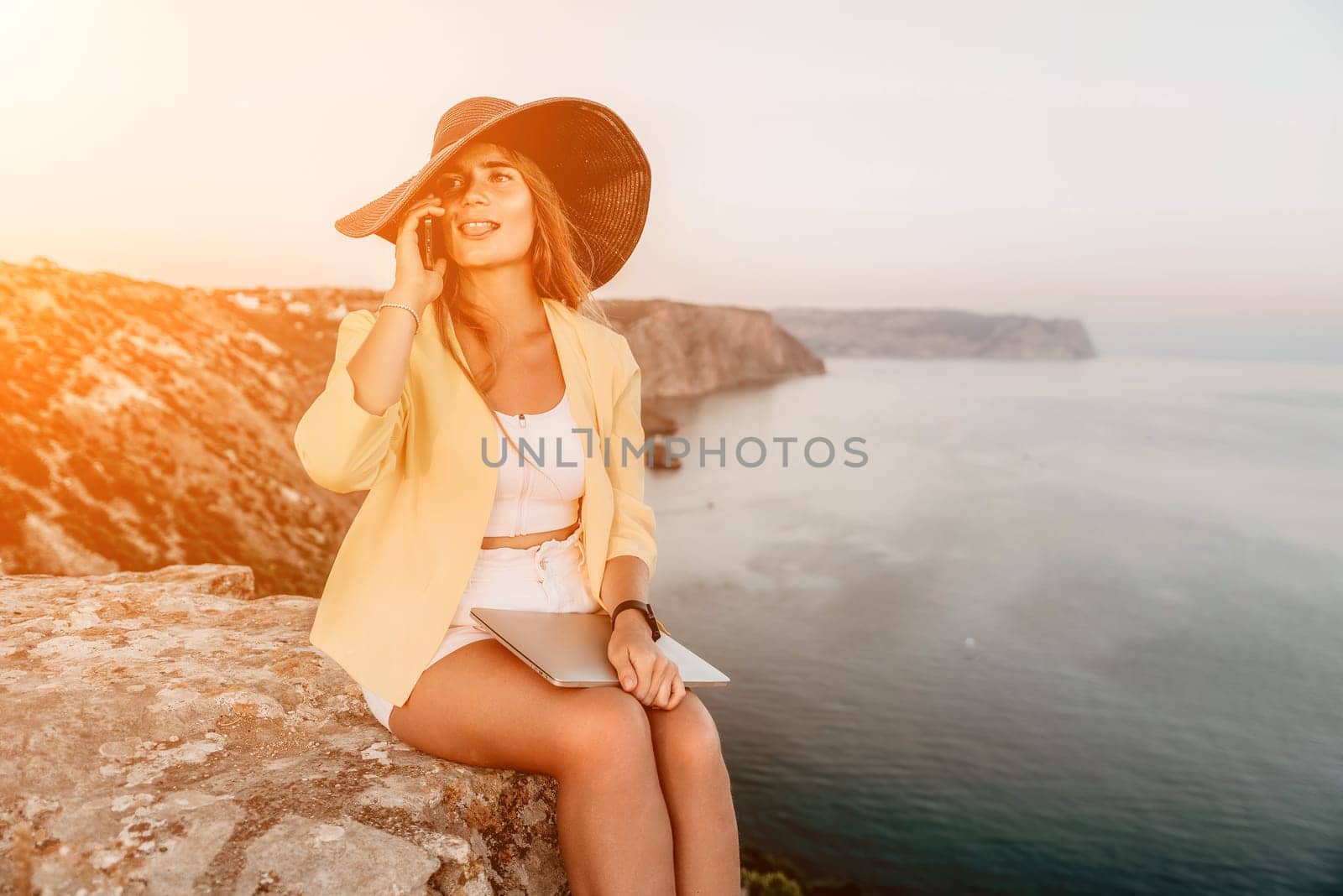 Digital nomad, Business woman working on laptop by the sea. Pretty lady typing on computer by the sea at sunset, makes a business transaction online from a distance. Freelance, remote work on vacation by panophotograph