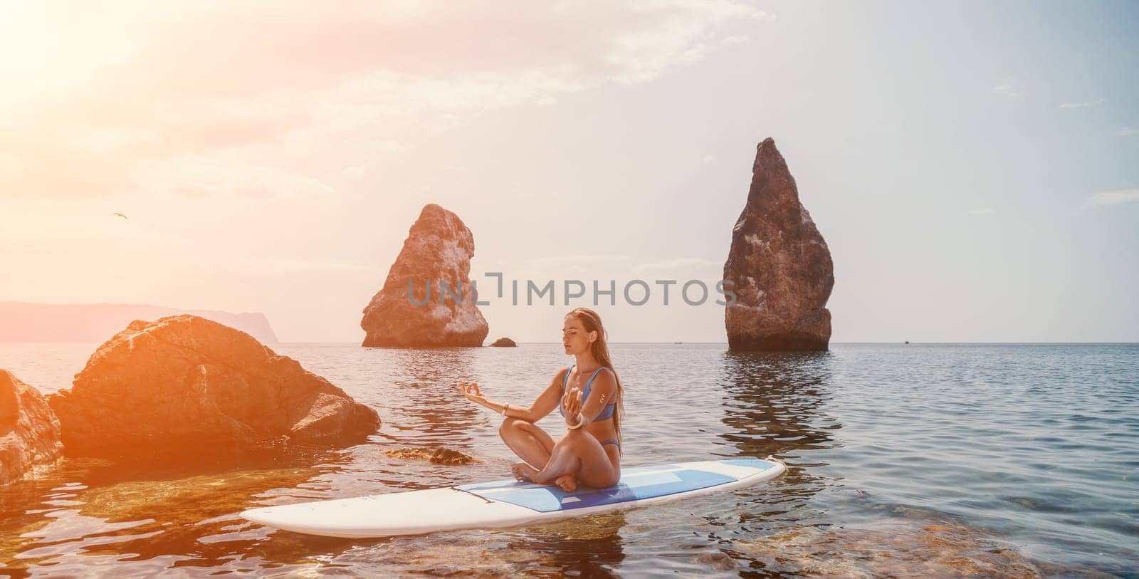 Woman sup yoga. Happy sporty woman practising yoga pilates on paddle sup surfboard. Female stretching doing workout on sea water. Modern individual female hipster outdoor summer sport activity. by panophotograph