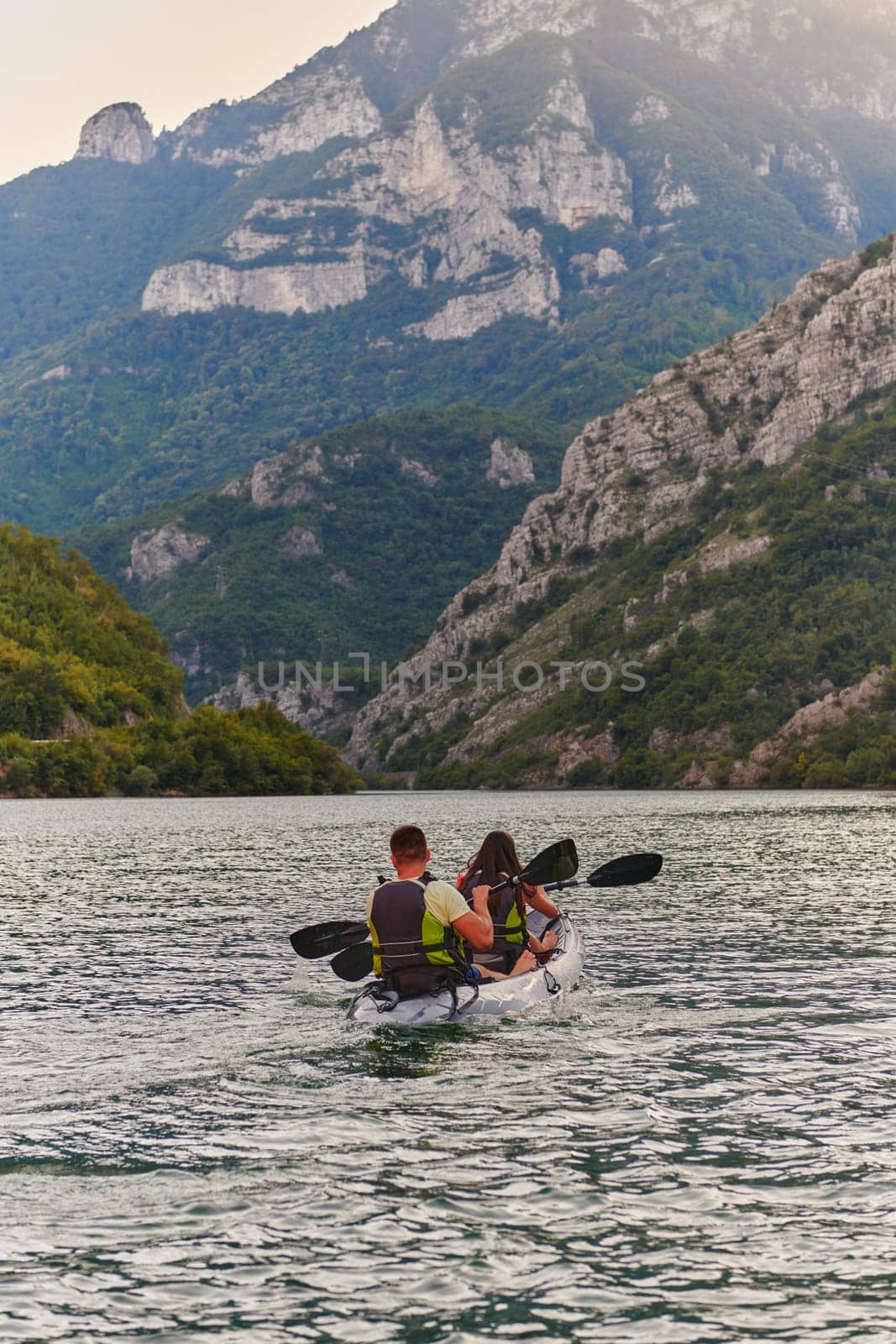 A young couple enjoying an idyllic kayak ride in the middle of a beautiful river surrounded by forest greenery in sunset time.