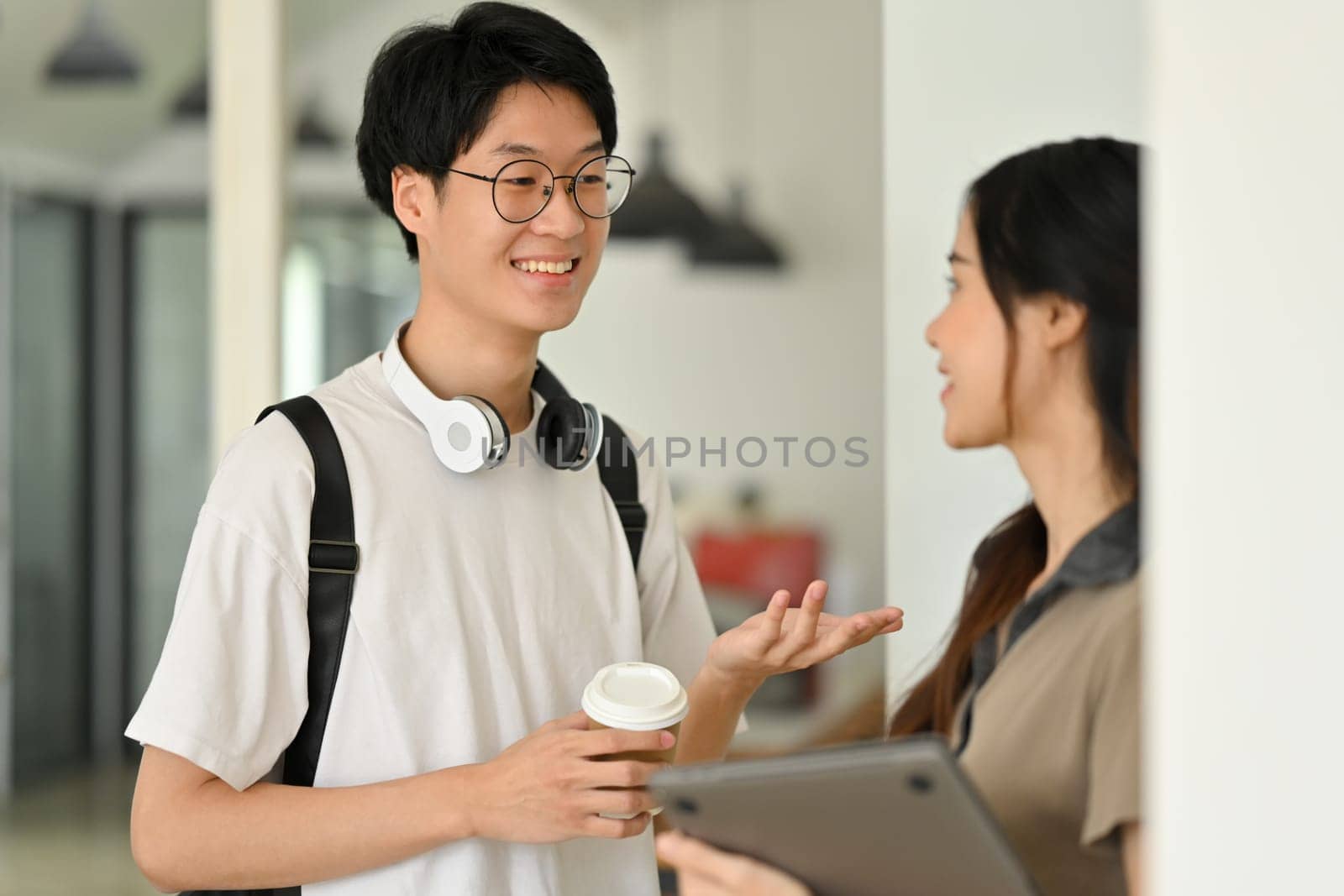 Smiling young student man talking with his classmate while standing at lockers. Youth lifestyle, University and Friend concept.