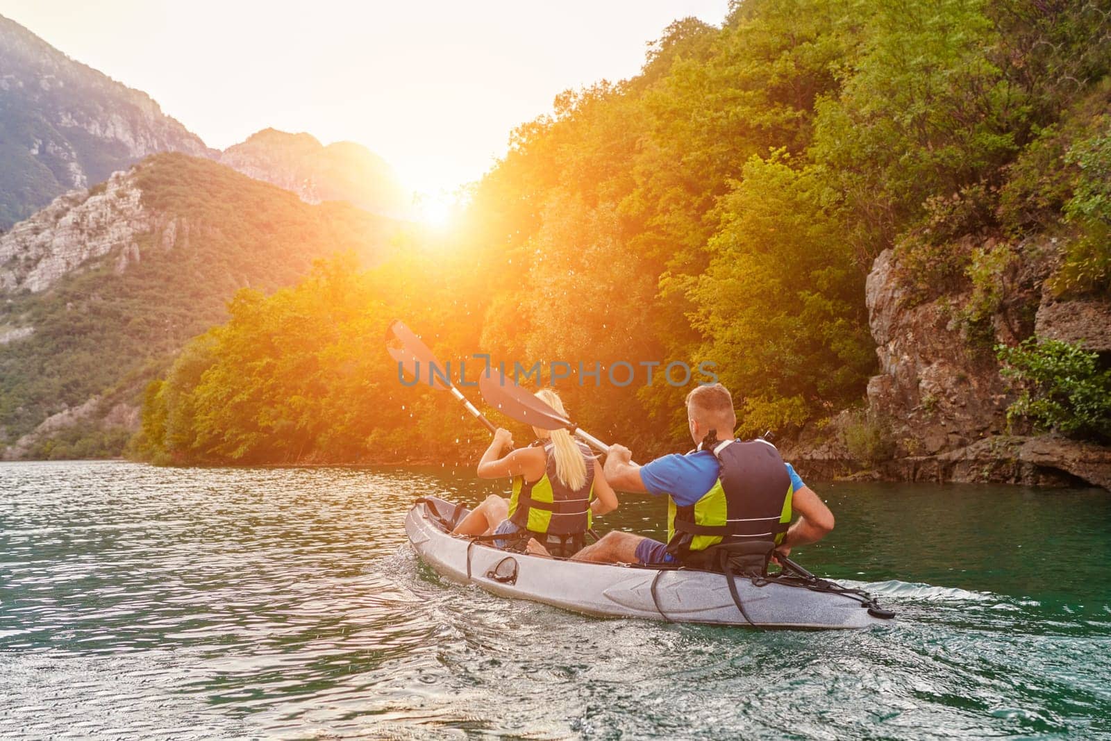 A group of friends enjoying fun and kayaking exploring the calm river, surrounding forest and large natural river canyons during an idyllic sunset. by dotshock