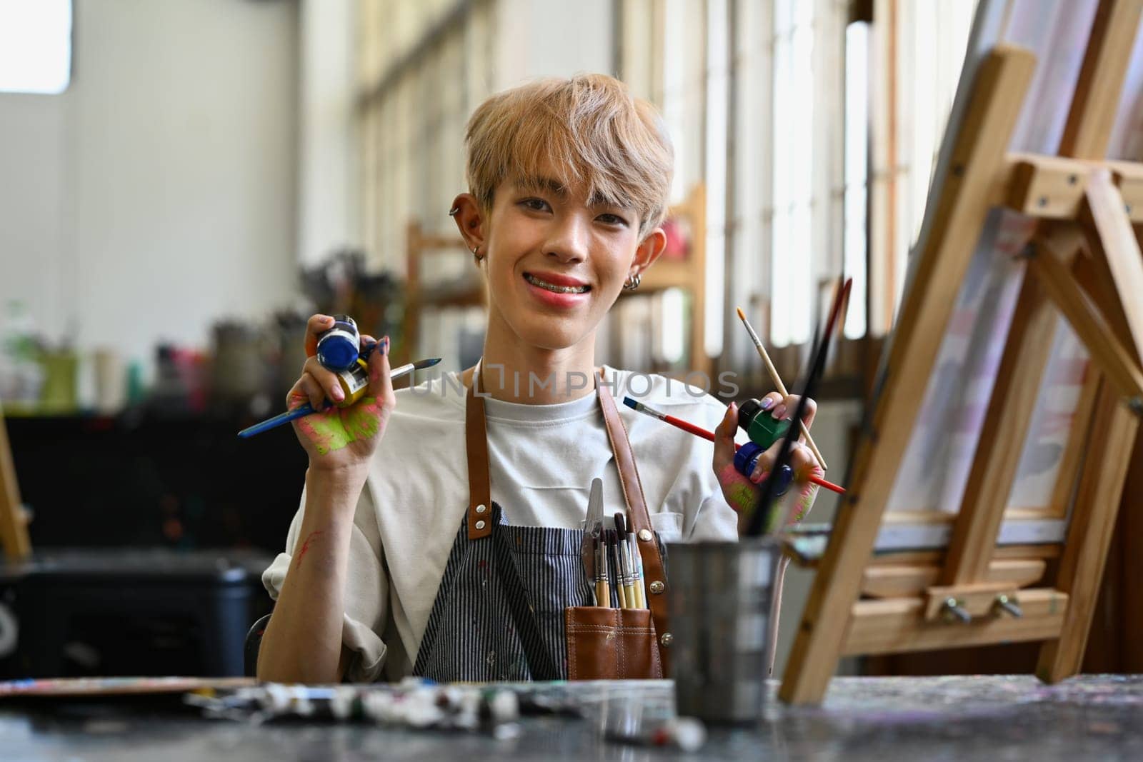 Smiling young Asian gay man enjoying creative activity, painting in art workshop. Hobby and leisure concept.