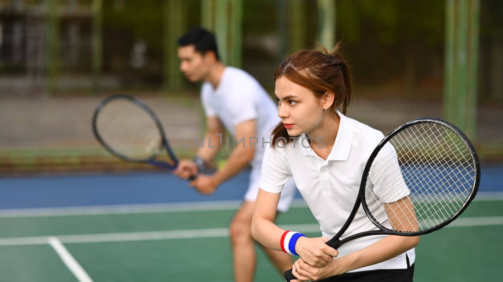 Focused female athlete with a racket waiting to receive ball during match at outdoor court by prathanchorruangsak