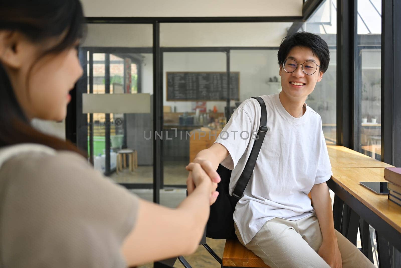 Smiling asian university student man shaking hands, greeting his friend.