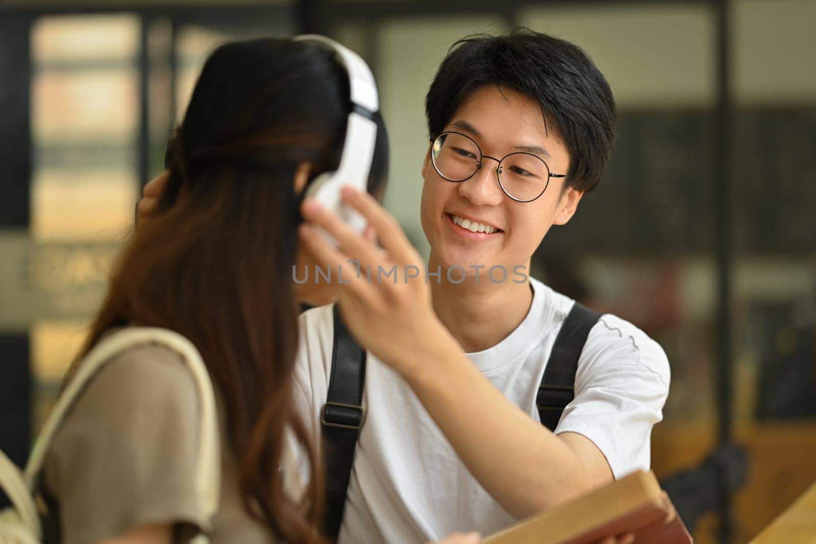 Smiling young asian man wearing headphones to his girlfriend. Lifestyle and love concept by prathanchorruangsak