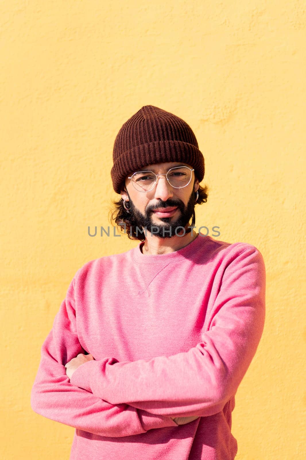 stylish young man smiling looking at camera with arms crossed in a yellow background, concept of youth and modern lifestyle, copy space for text