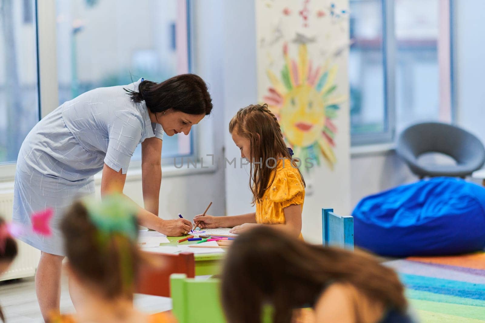 Creative kids during an art class in a daycare center or elementary school classroom drawing with female teacher