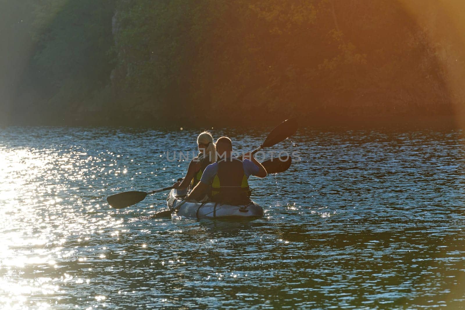 A young couple enjoying an idyllic kayak ride in the middle of a beautiful river surrounded by forest greenery in sunset time by dotshock