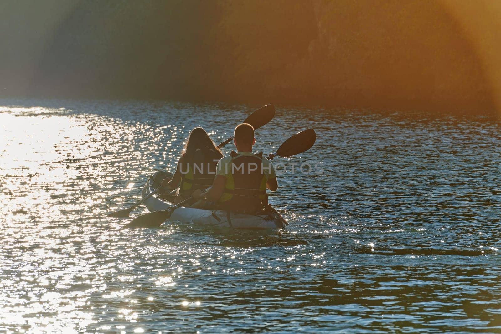 A young couple enjoying an idyllic kayak ride in the middle of a beautiful river surrounded by forest greenery in sunset time by dotshock