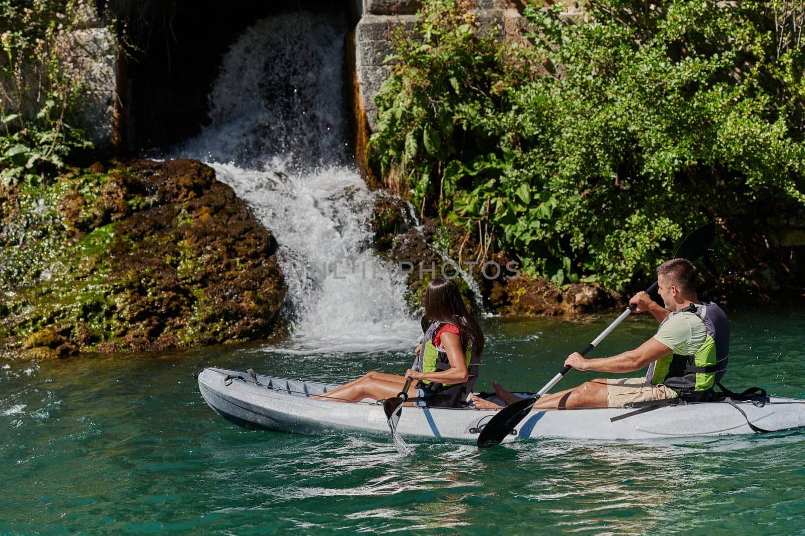 A young couple enjoying an idyllic kayak ride in the middle of a beautiful river surrounded by forest greenery by dotshock