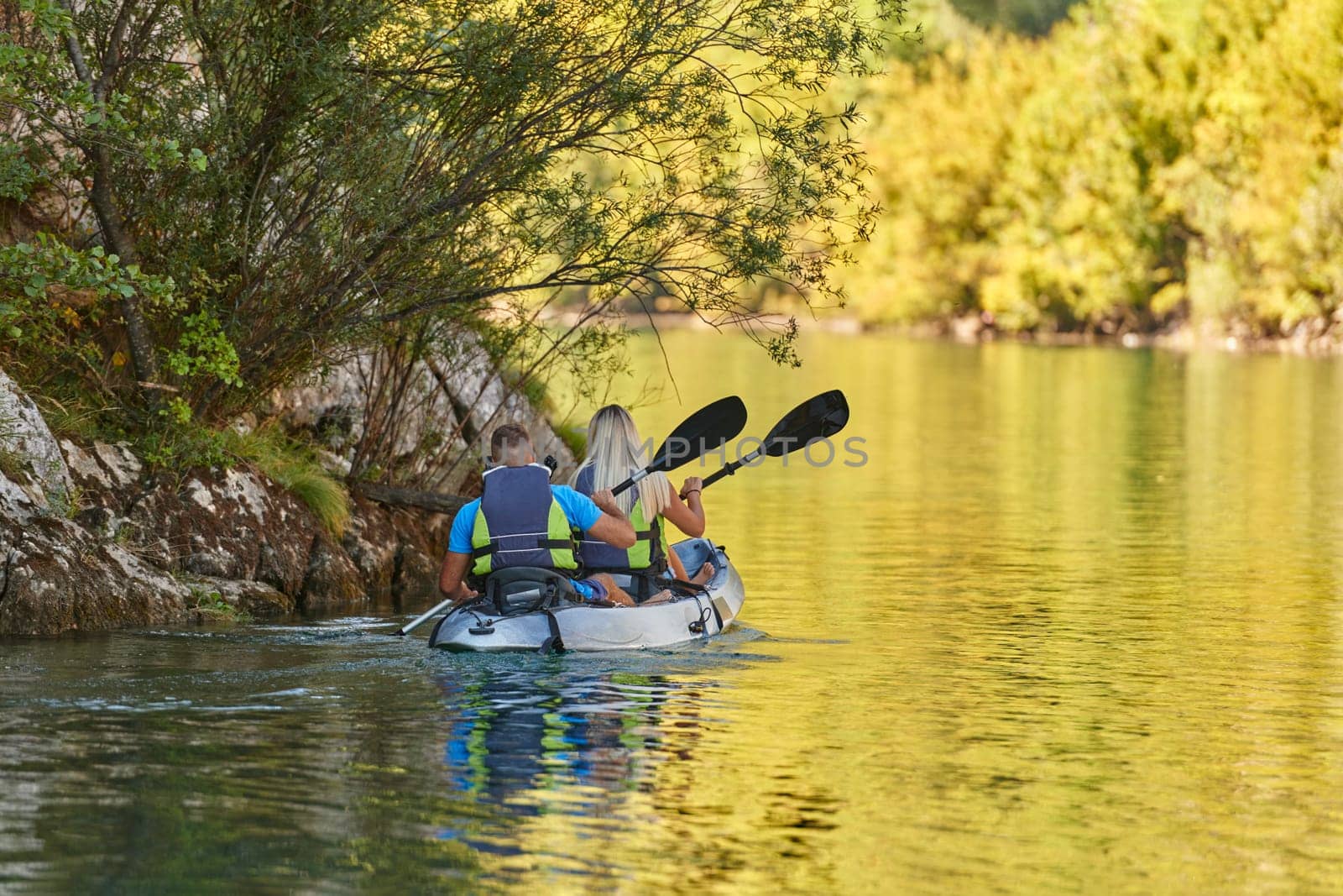 A young couple enjoying an idyllic kayak ride in the middle of a beautiful river surrounded by forest greenery by dotshock