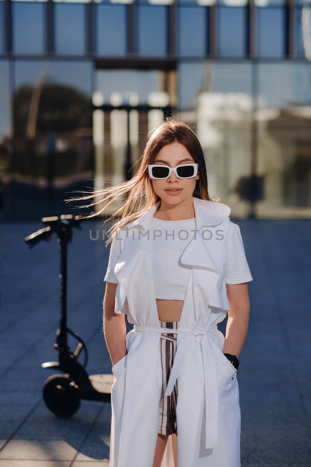 Stylish girl in glasses and a white summer coat in the city.