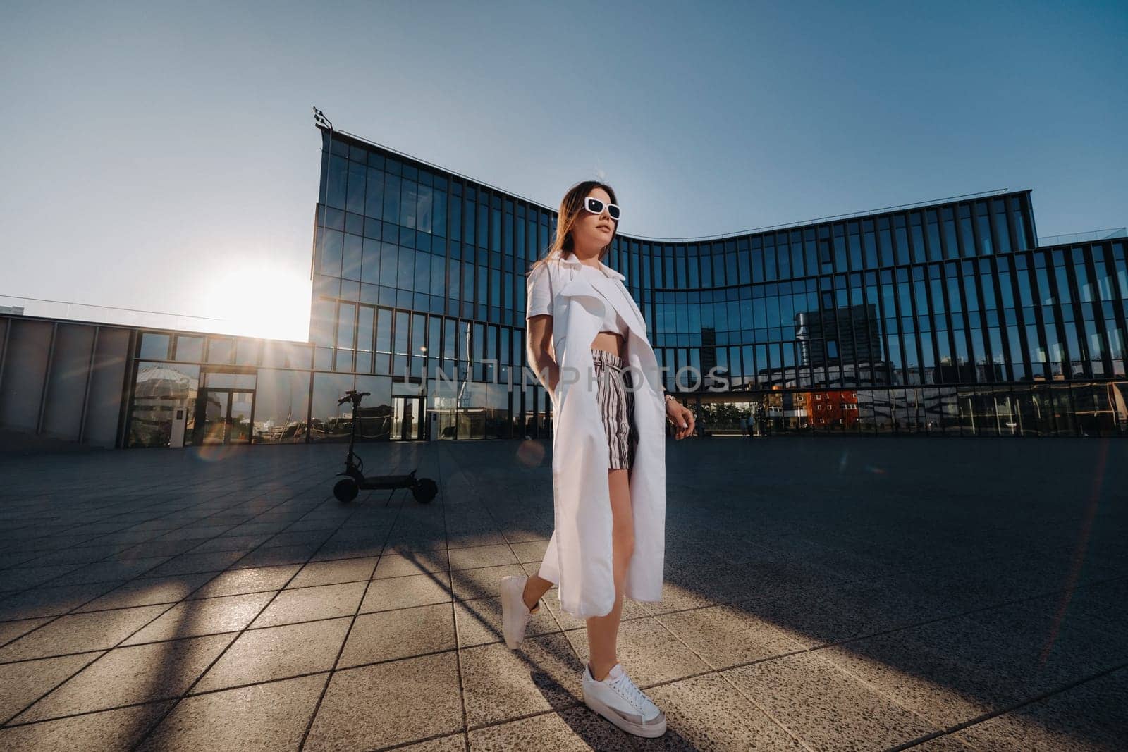 Stylish girl in glasses and a white summer coat in the city.