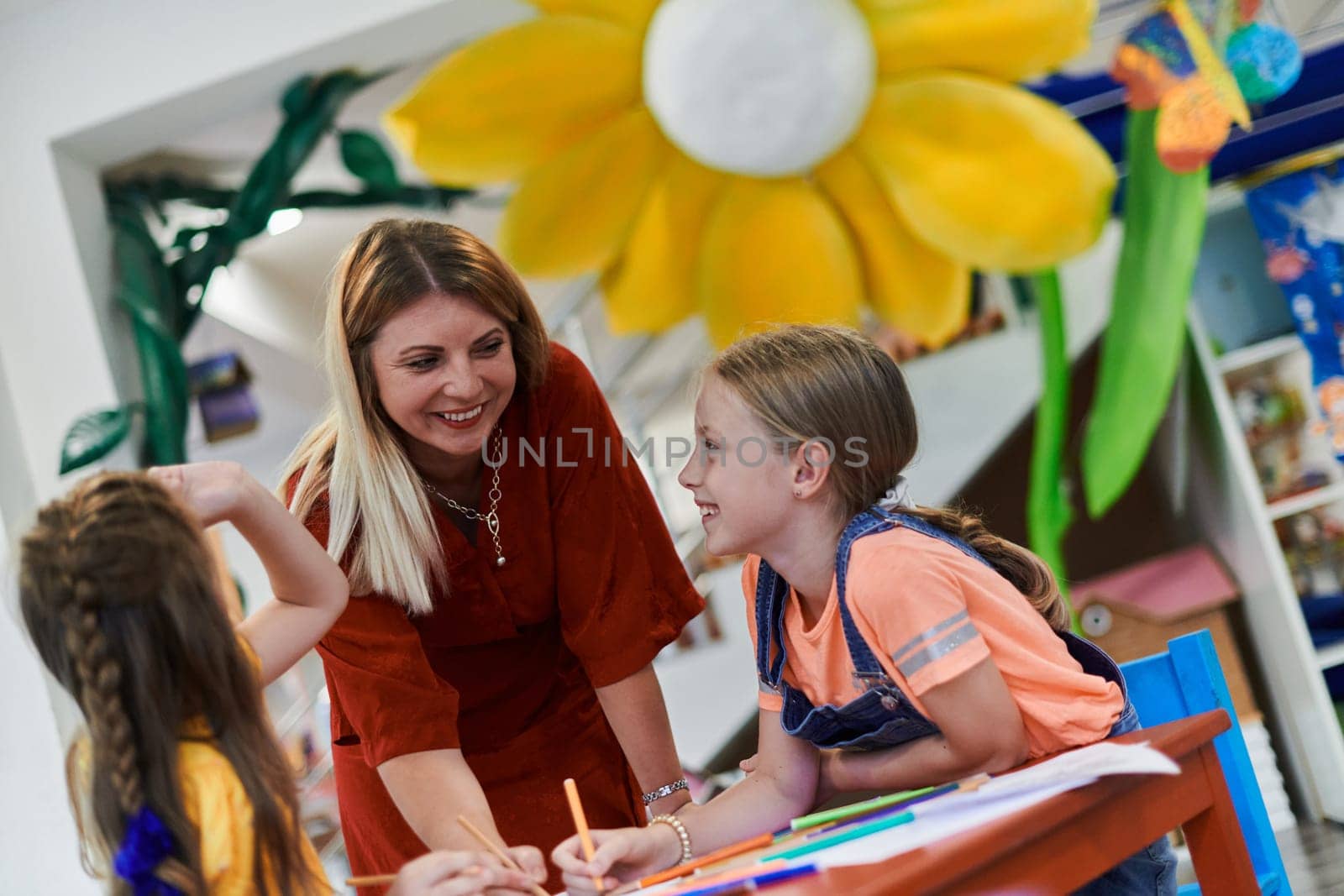 Creative kids during an art class in a daycare center or elementary school classroom drawing with female teacher