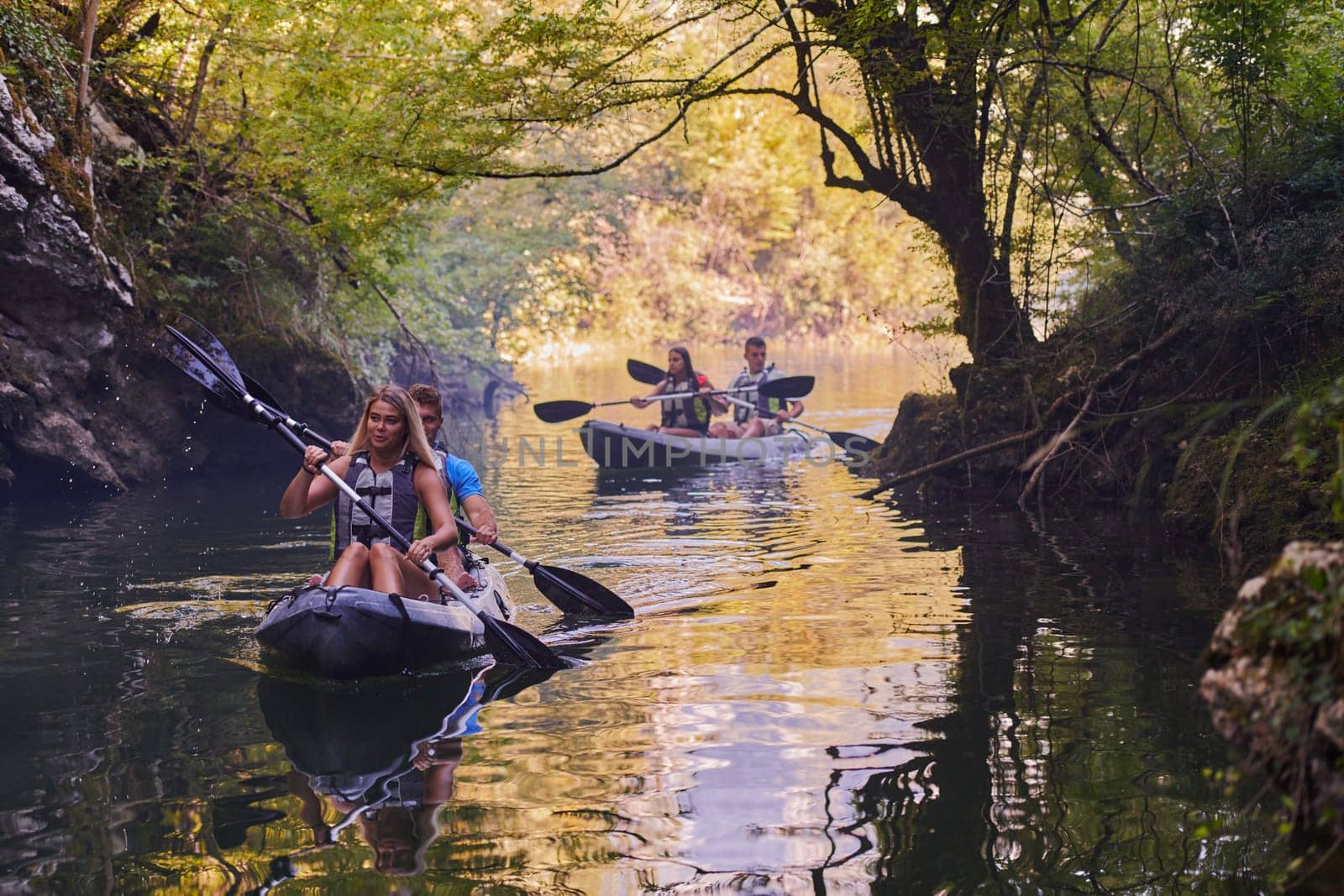 A group of friends enjoying having fun and kayaking while exploring the calm river, surrounding forest and large natural river canyons.