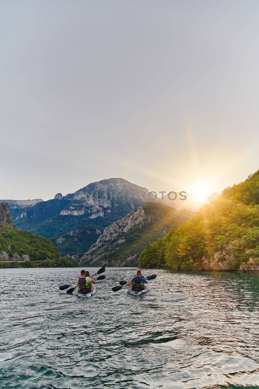 A group of friends enjoying fun and kayaking exploring the calm river, surrounding forest and large natural river canyons during an idyllic sunset