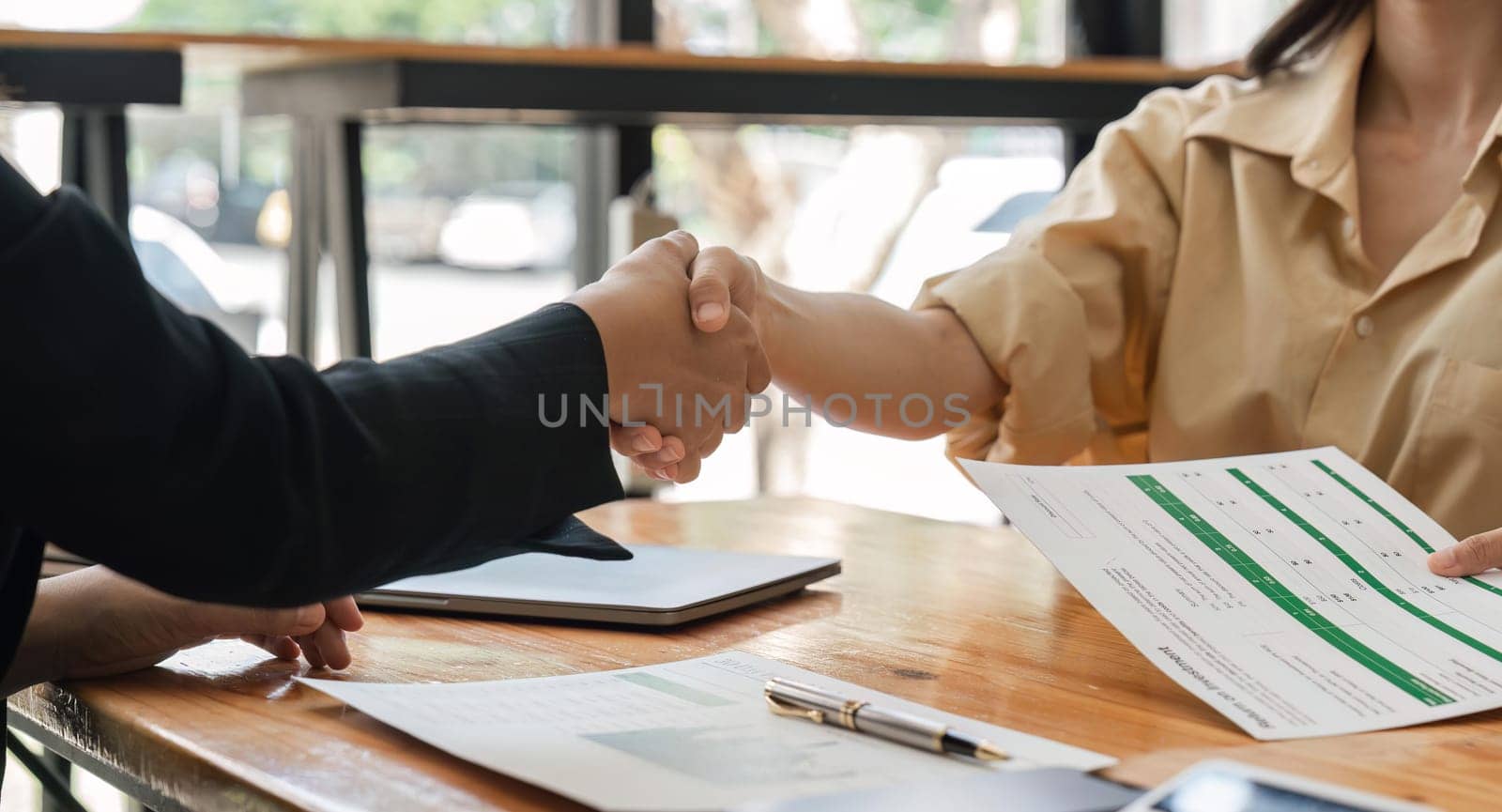 businesspeople shake hand after their partnerships in conference room and finalized pile of papers of financial report and data analysis on meeting table.