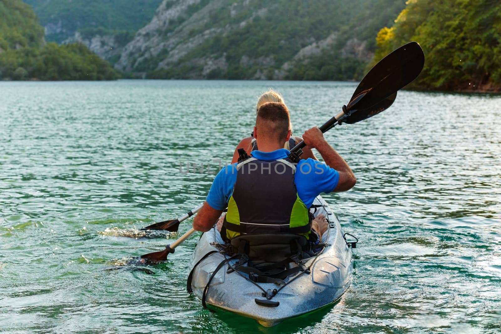 A young couple enjoying an idyllic kayak ride in the middle of a beautiful river surrounded by forest greenery in sunset time.