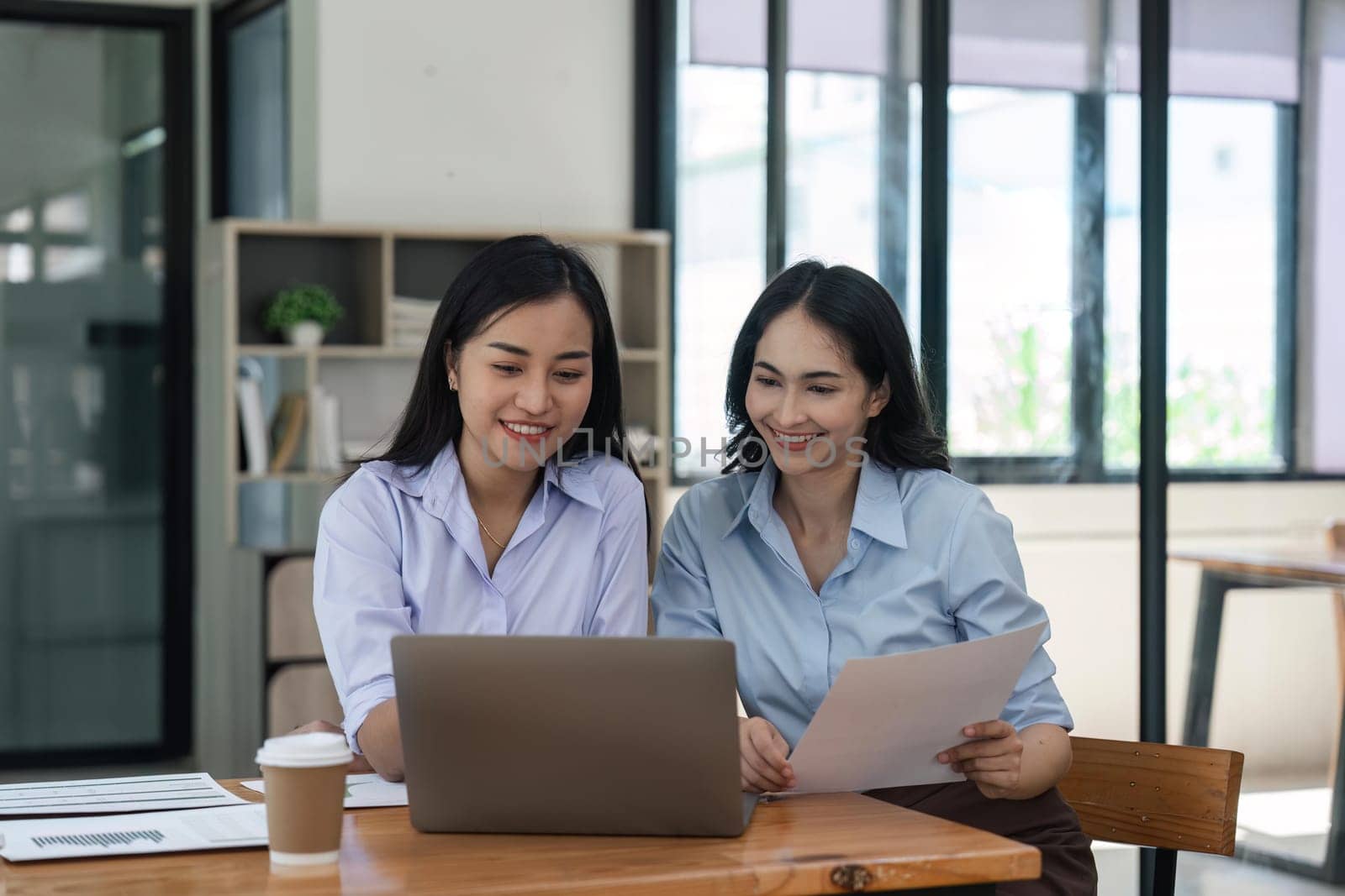 Happy two beautiful young Asian businesswoman standing discuss working together at office by nateemee