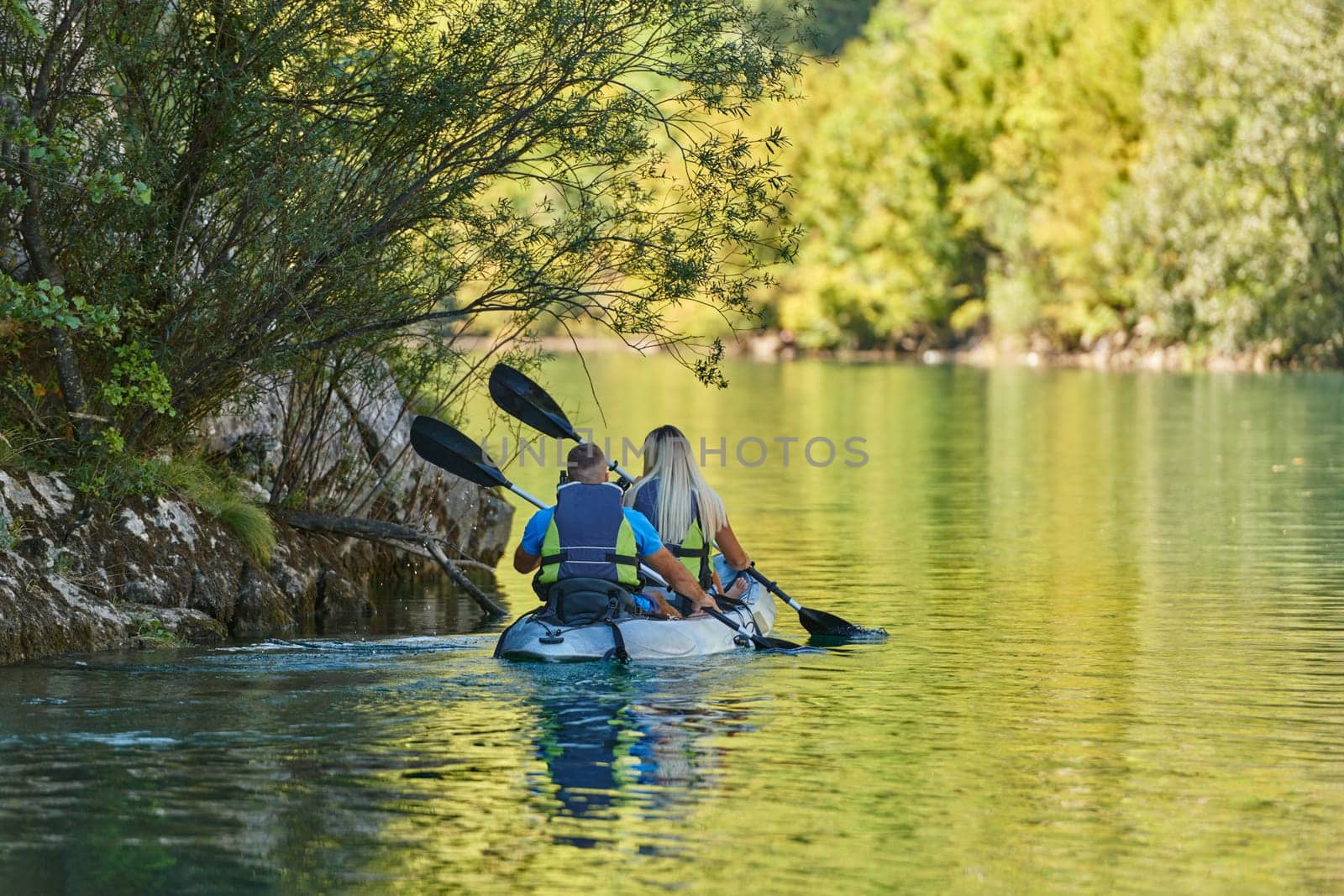 A young couple enjoying an idyllic kayak ride in the middle of a beautiful river surrounded by forest greenery.