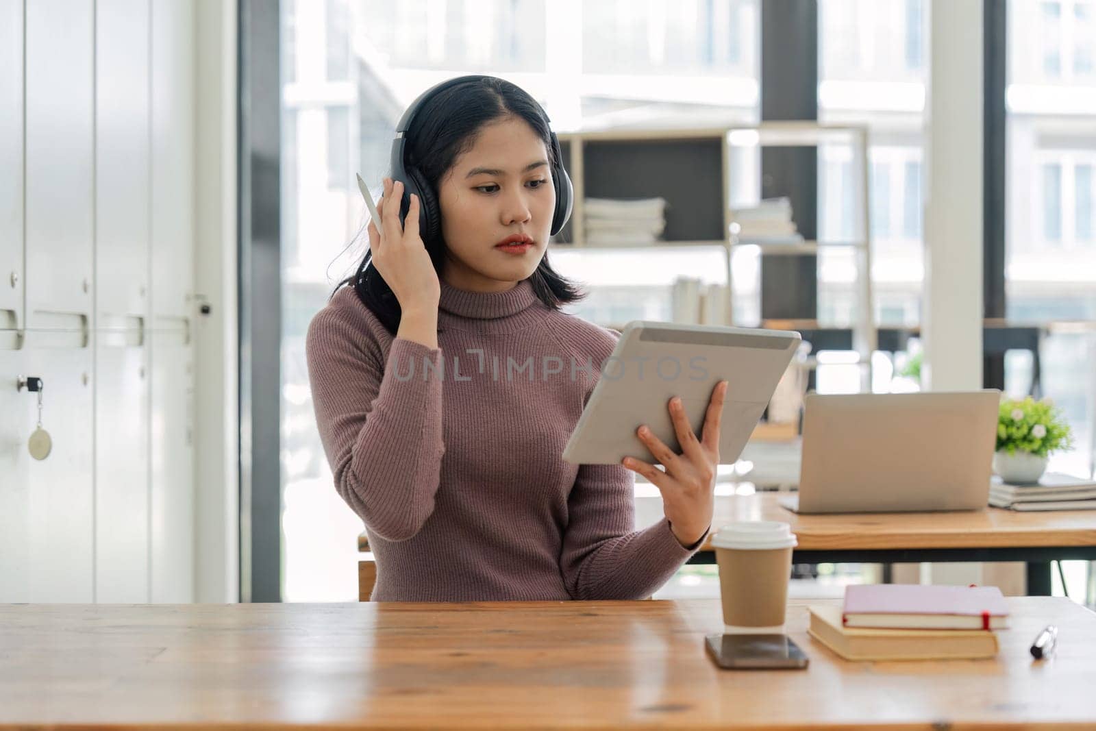 Asian girl college student wearing headphones taking online training class on digital tablet sitting at university table. Virtual education webinar, remote study, distance academic learning.