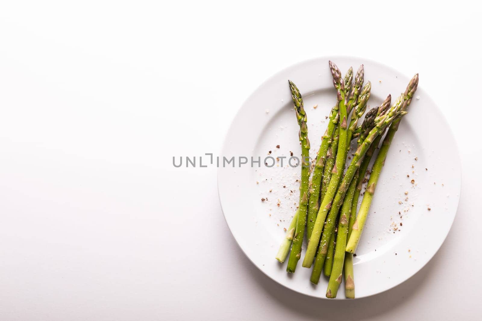 Overhead view of asparagus and seasoning in plate by copy space against white background. unaltered, food, healthy eating and organic concept.