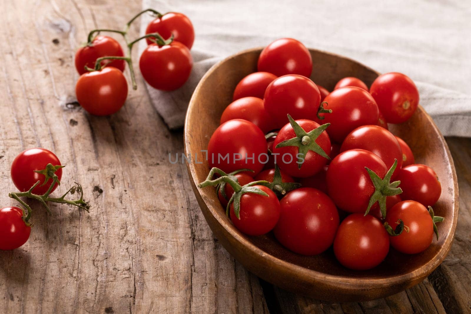 High angle view of fresh red cherry tomatoes in bowl on wooden table. unaltered, organic food and healthy eating concept.