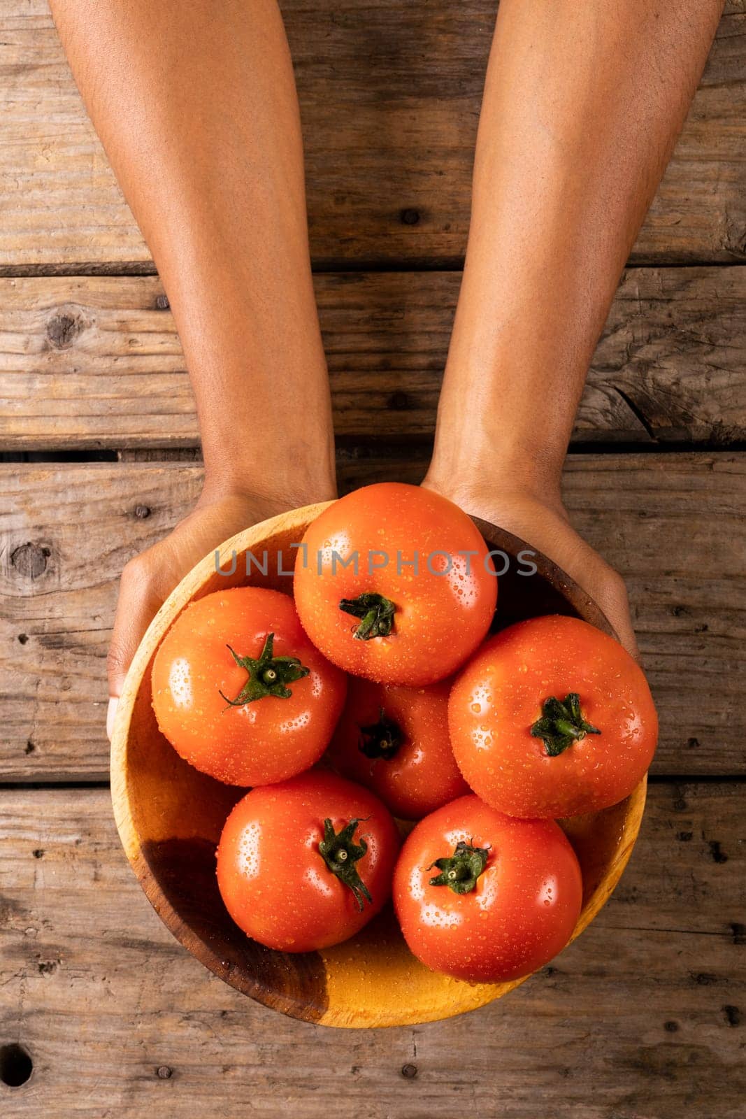 Overhead view of man's hands holding bowl full of fresh tomatoes in bowl on wooden table. unaltered, organic food and healthy eating concept.