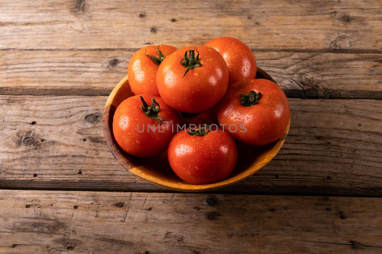 High angle view of fresh red tomatoes with water drops in bowl on wooden table. unaltered, organic food and healthy eating concept.