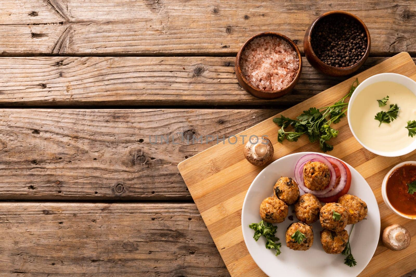 Directly above view of fresh meatballs with seasoning bowls on cutting board over wooden table by Wavebreakmedia