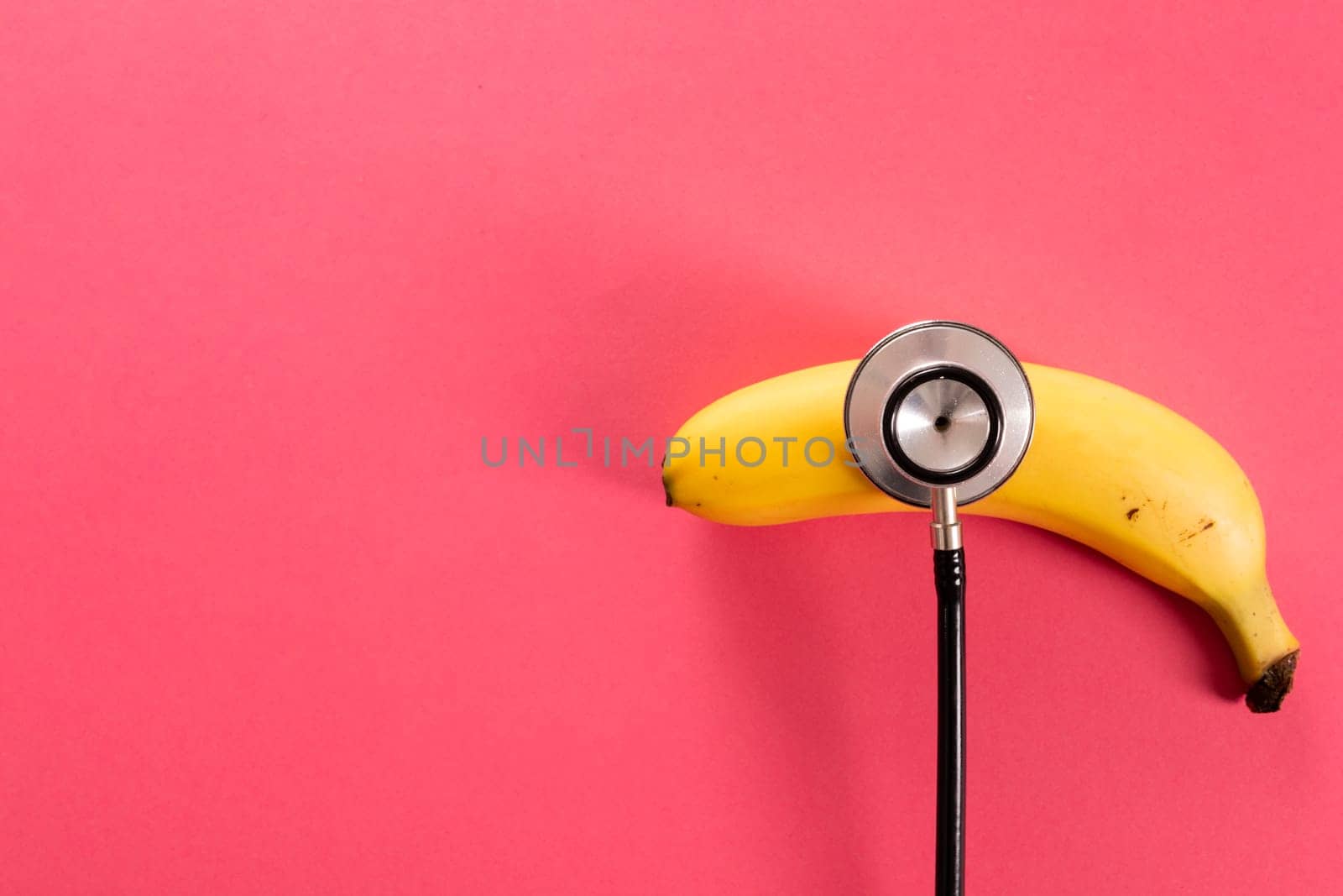 Overhead view of fresh banana with stethoscope by copy space over pink background. unaltered, organic food, healthy eating and medical equipment concept.