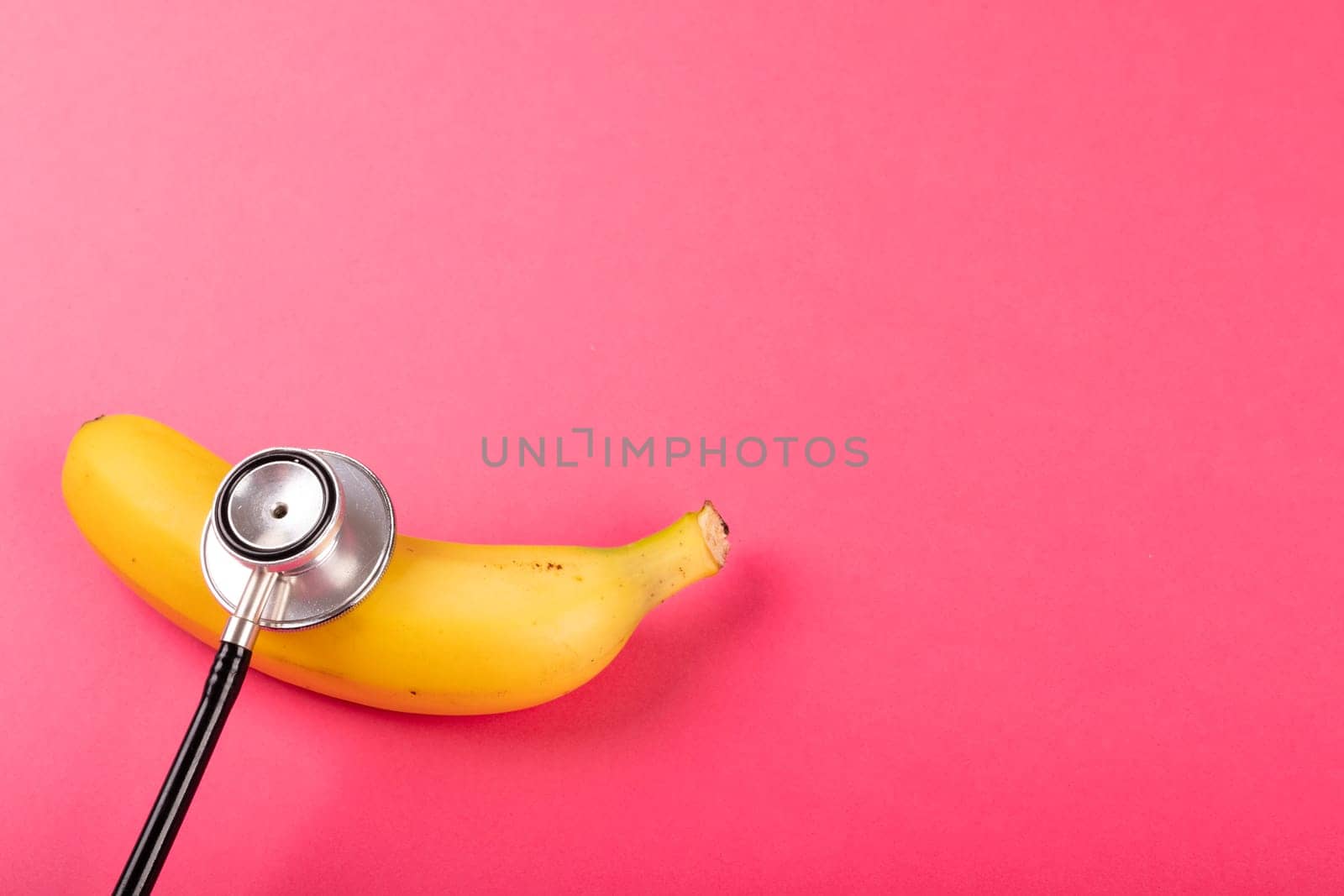 Directly above view of fresh banana with stethoscope by copy space on pink background. unaltered, organic food, healthy eating and medical equipment concept.