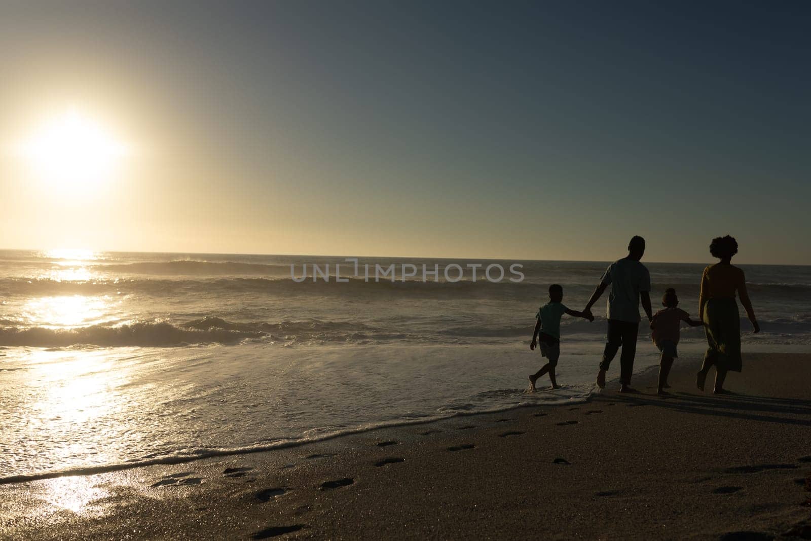 African american family walking while holding hands at beach with copy space during sunset. unaltered, family, lifestyle, togetherness, enjoyment and holiday concept.