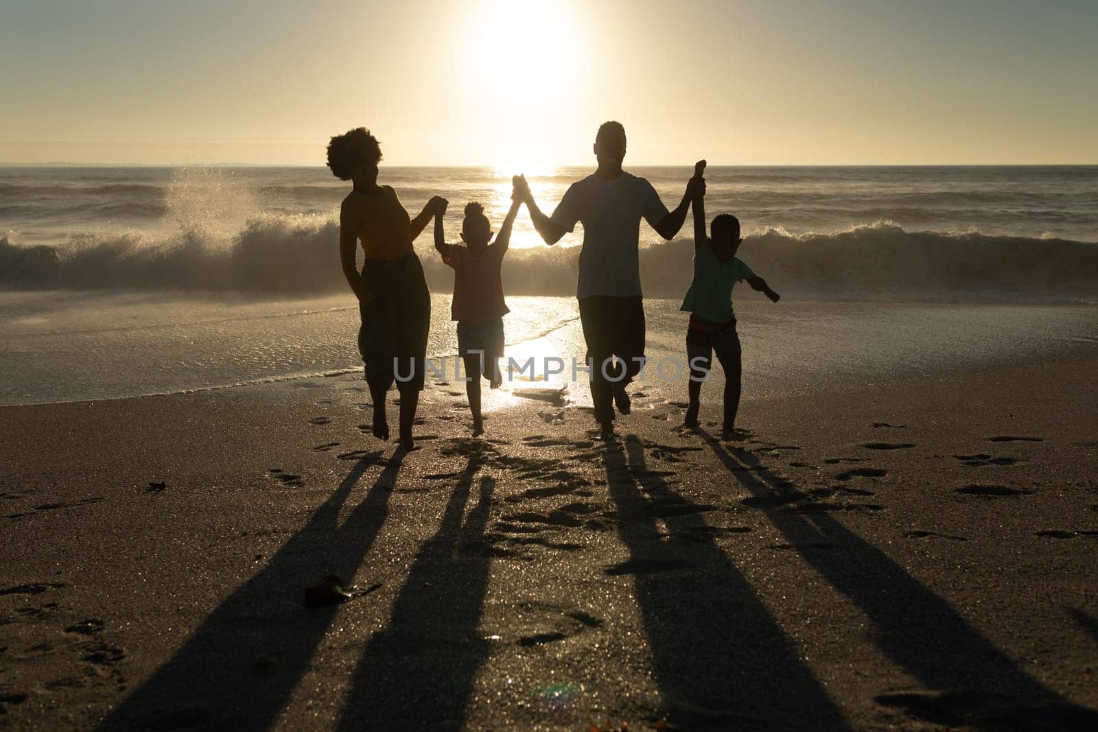 Happy african american parents enjoying sunset with children at beach against sky by Wavebreakmedia