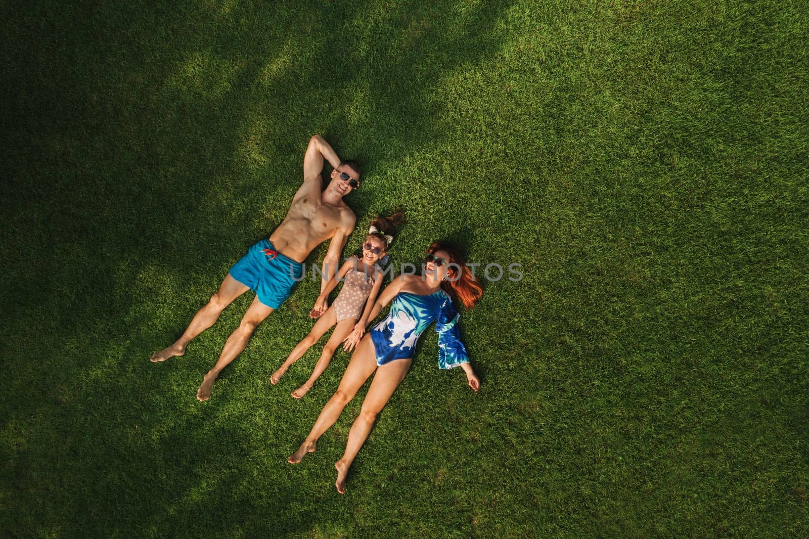 Top view of a happy family in swimsuits lying on the green grass.