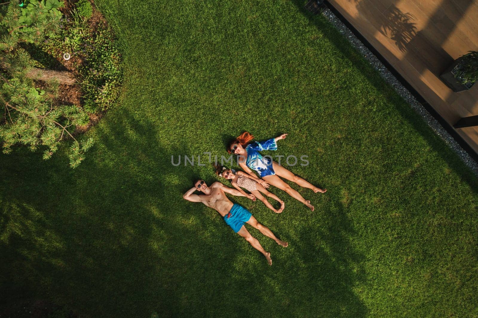 Top view of a happy family in swimsuits lying on the green grass by Lobachad