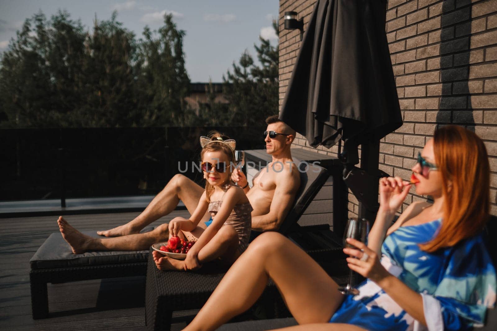 A happy family in swimsuits sunbathe in summer on their terrace on sun beds.