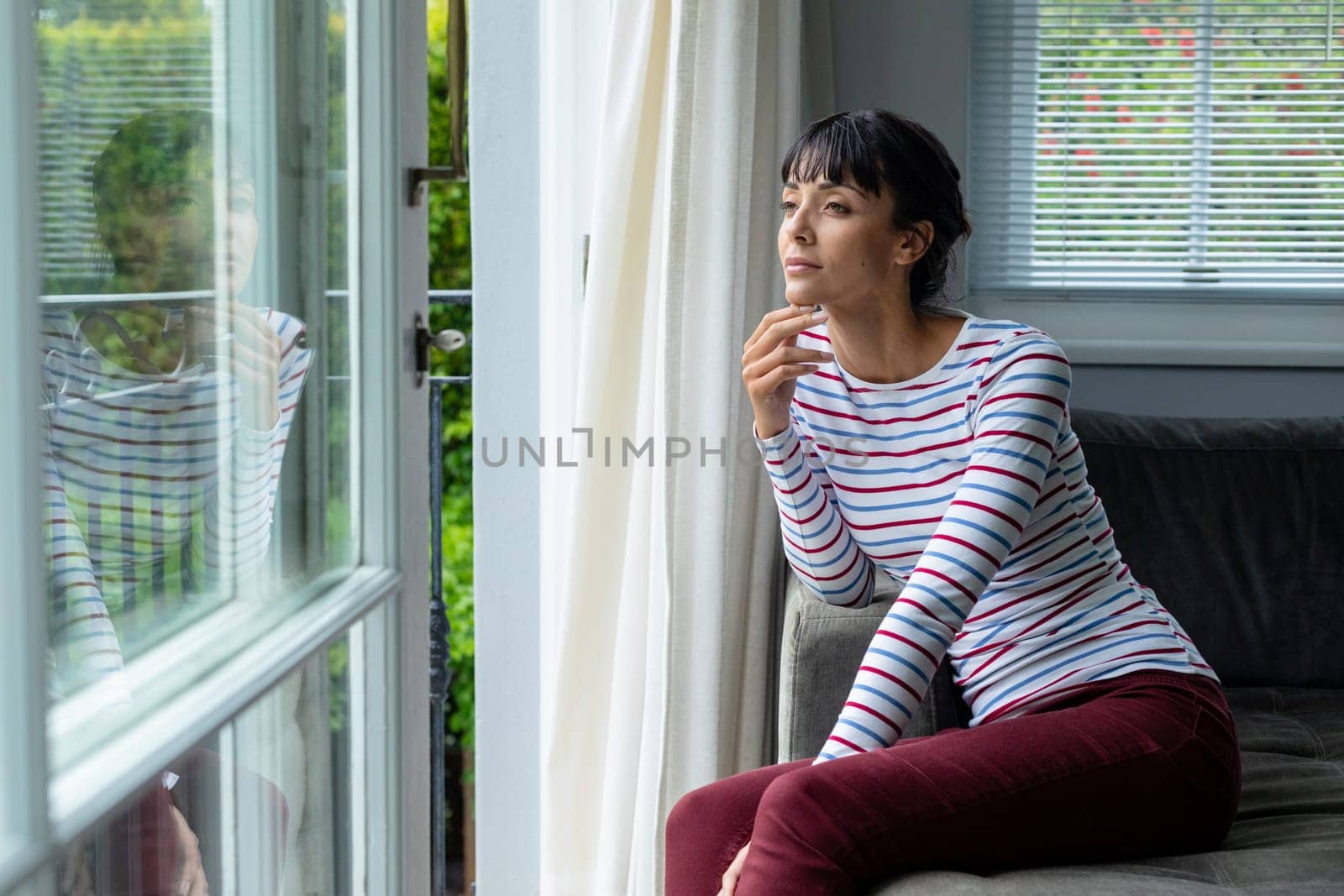 Thoughtful caucasian young woman looking through window while sitting at home by Wavebreakmedia