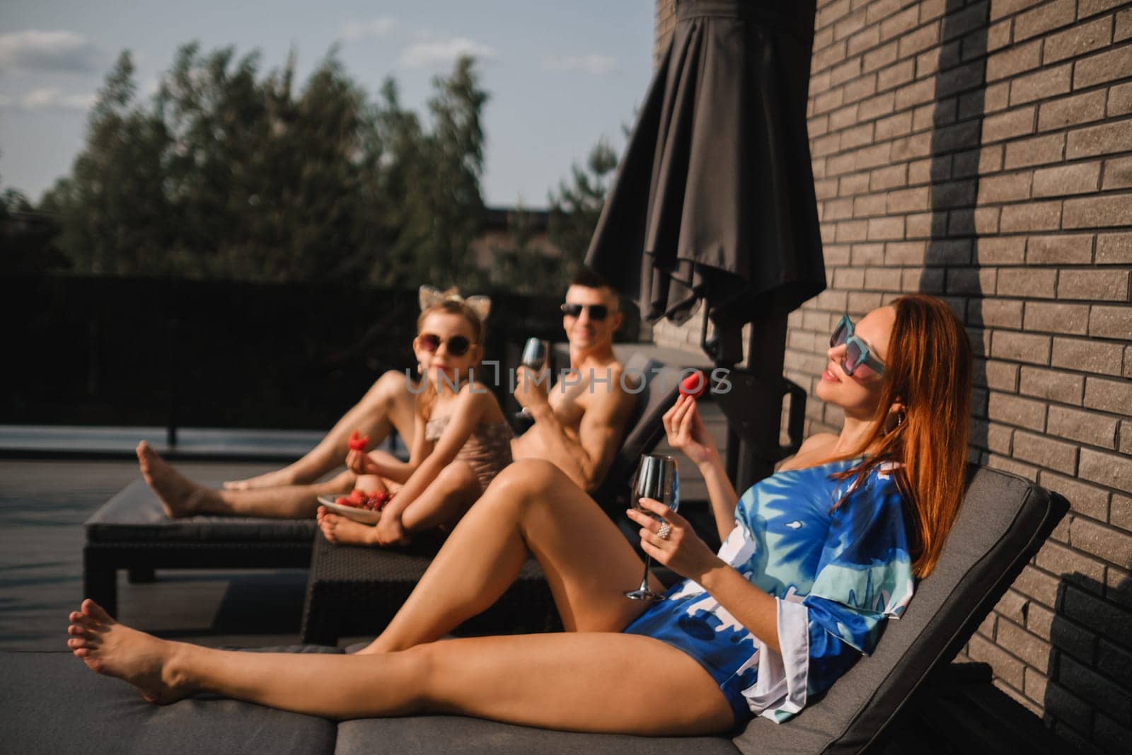 A happy family in swimsuits sunbathe in summer on their terrace on sun beds by Lobachad