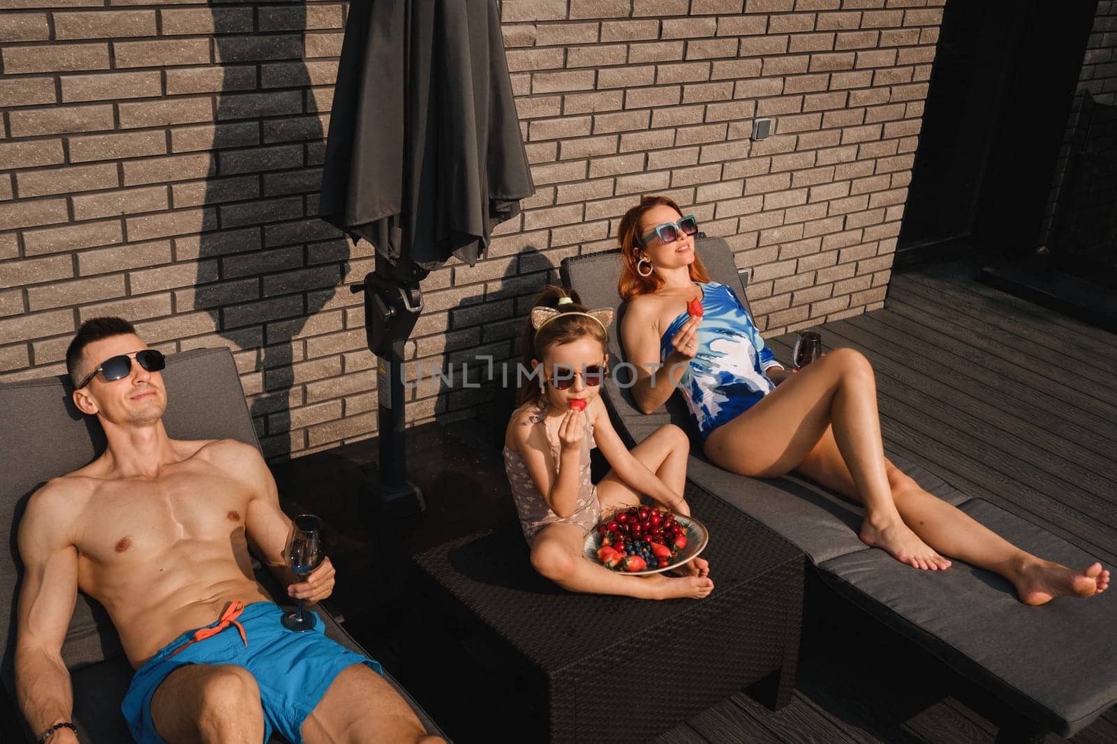 A happy family in swimsuits sunbathe in summer on their terrace on sun beds.