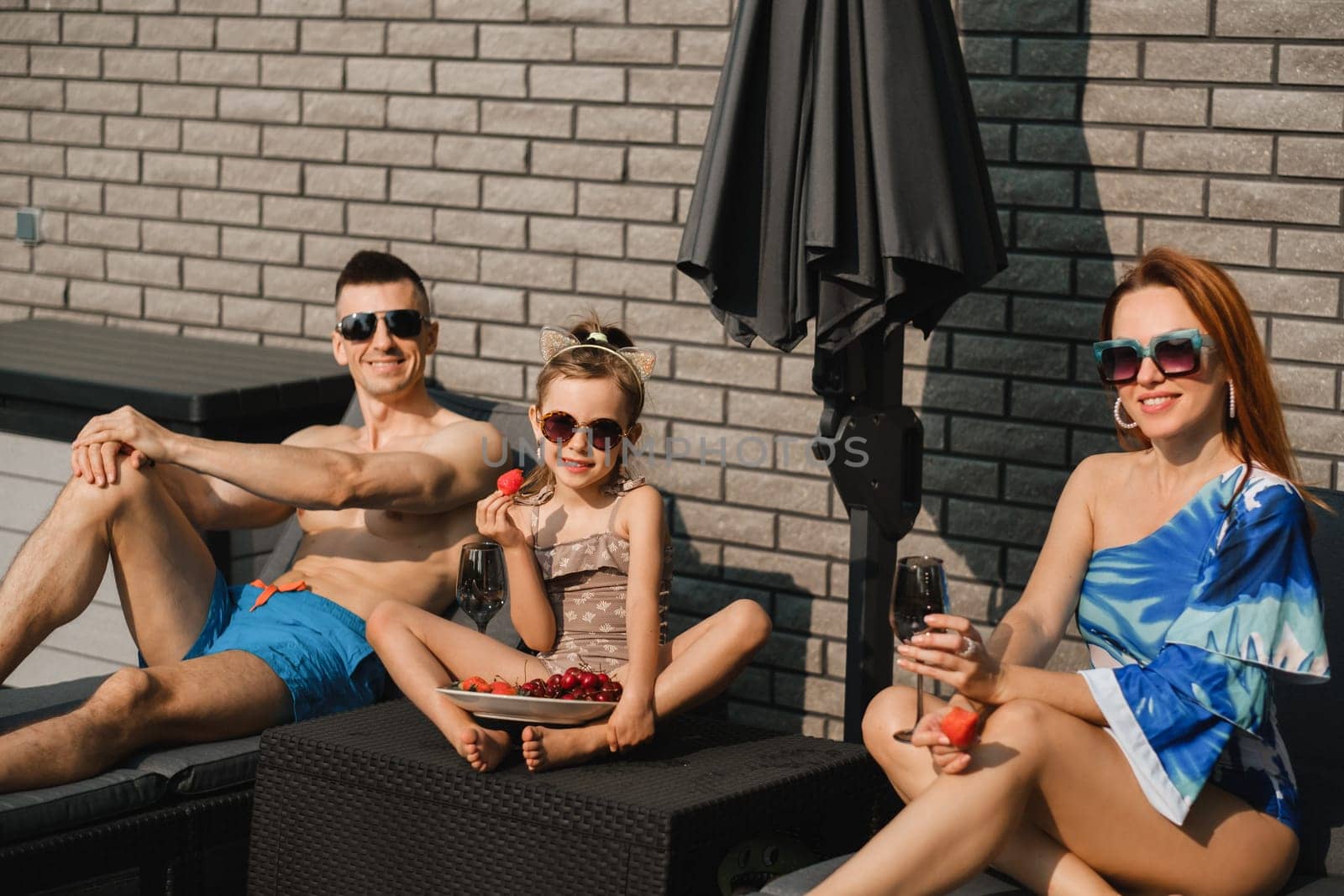 A happy family in swimsuits sunbathe in summer on their terrace on sun beds.