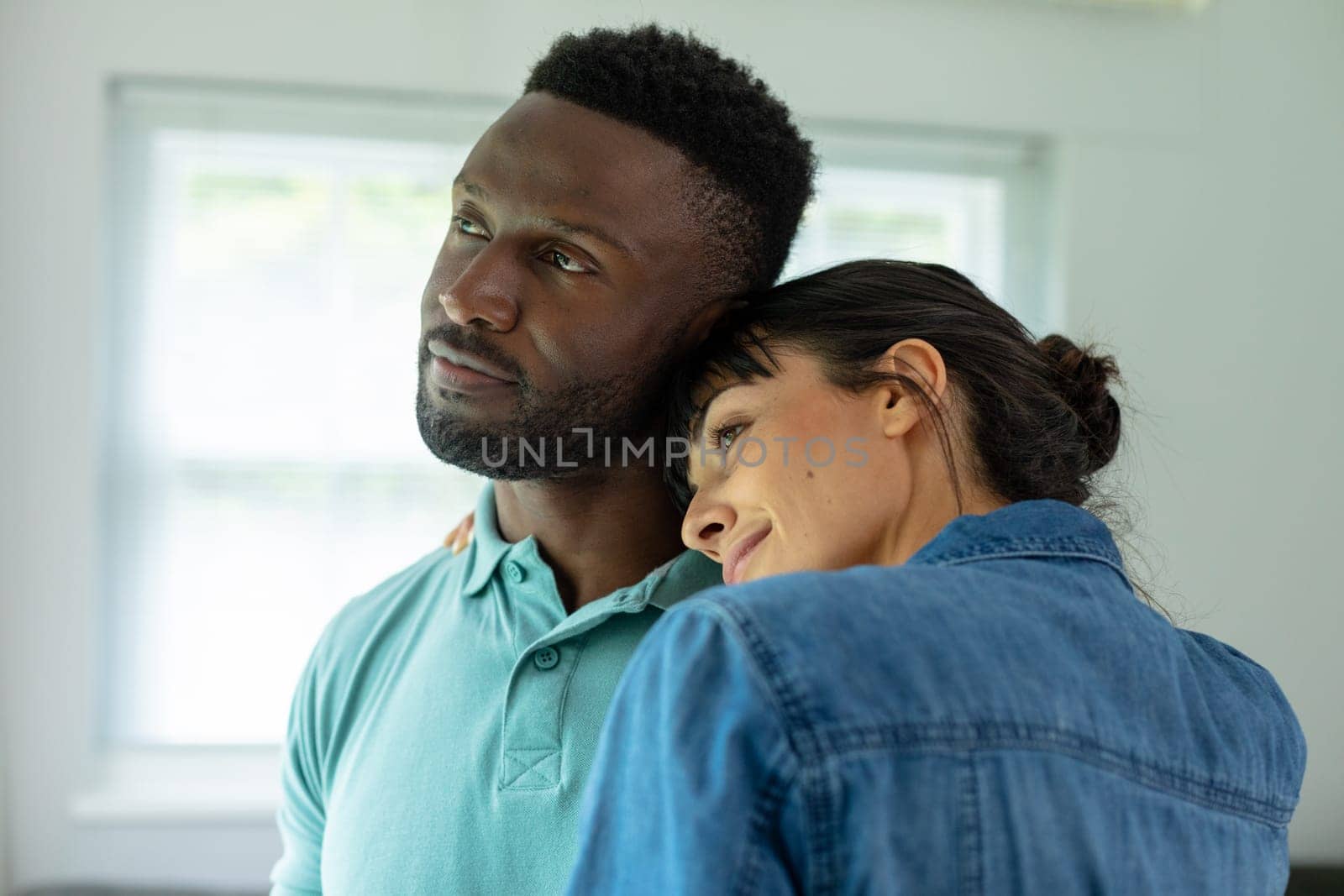 Multiracial young couple looking away while embracing in living room at home. unaltered, lifestyle, domestic life, togetherness, love, contemplation.