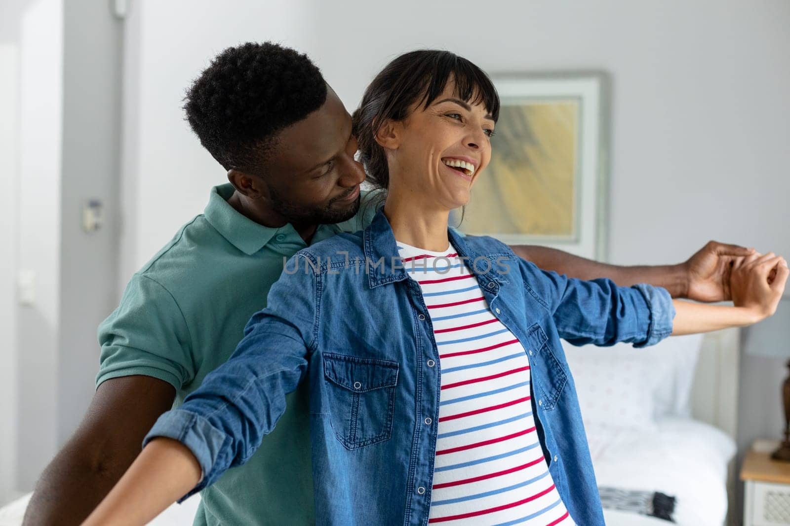 Happy multiracial young couple with arms outstretched standing in living room at home by Wavebreakmedia