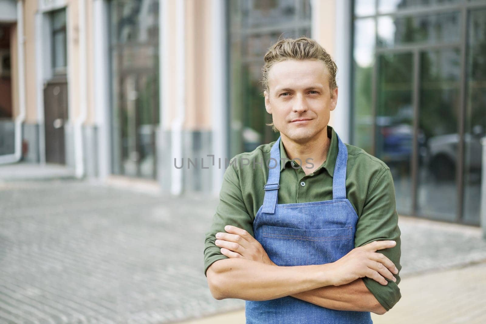 Restaurant or kitchen worker wearing blue apron, standing against backdrop of city. Concept of service and readiness to help. Customer service-oriented nature of the hospitality industry. . High quality photo